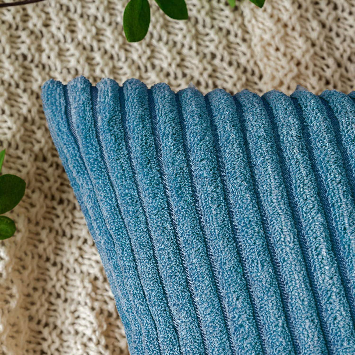 Eine Nahaufnahme eines strukturierten blauen Kissens auf einem gestrickten beigen Hintergrund mit nahegelegenen grünen Blättern, die eine gemütliche und natürliche Atmosphäre schaffen.