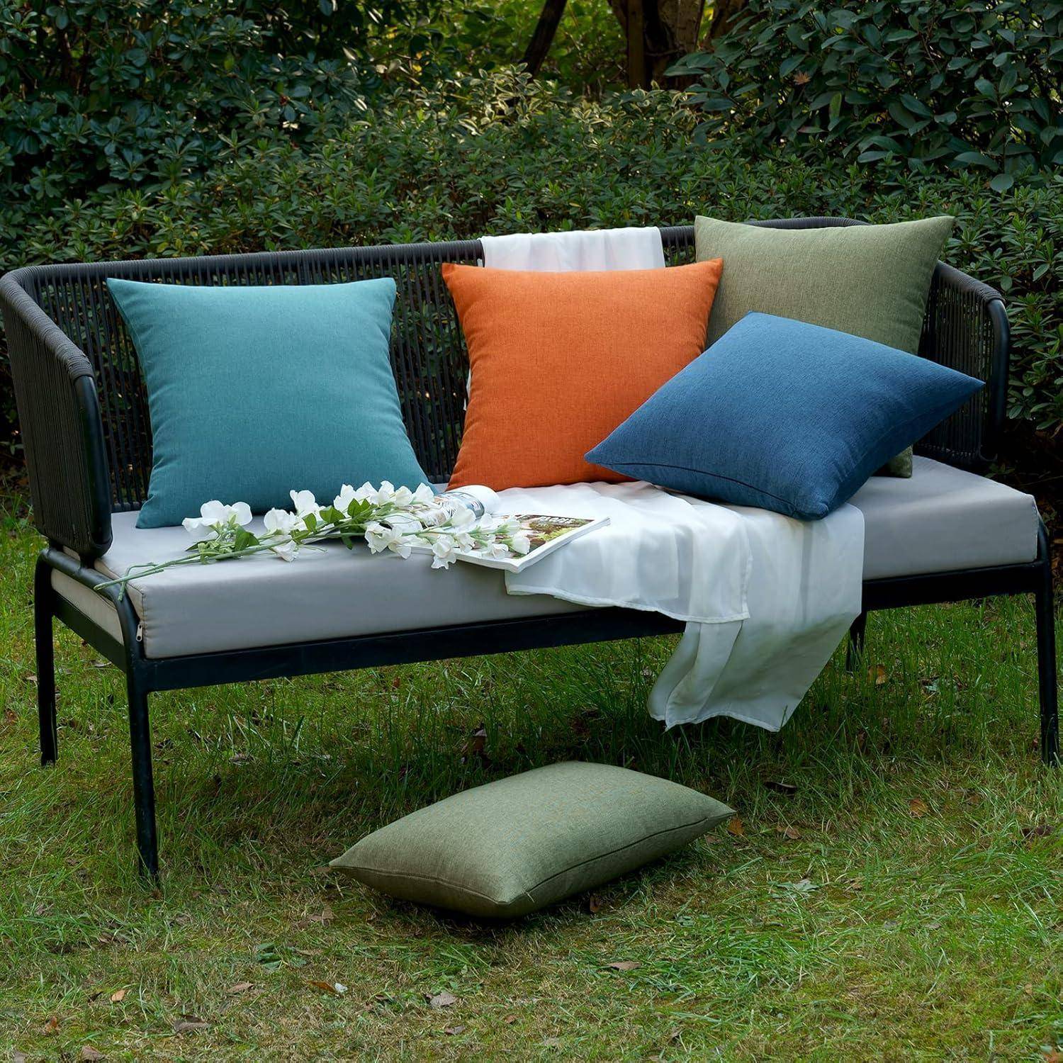 Outdoor-Gartenbank mit einem weißen Kissen, geschmückt mit vier farbenfrohen Kissen in Petrol, Orange, Blau und Hellgrün. Eine Pflanze sitzt auf der Bank.
