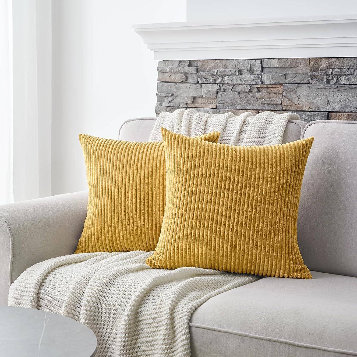 Ein hellgrauer Sofa mit zwei senfgelben Zierkissen und einer strukturierten beigen Decke darüber drapiert. Eine Steinakzentwand befindet sich im Hintergrund.