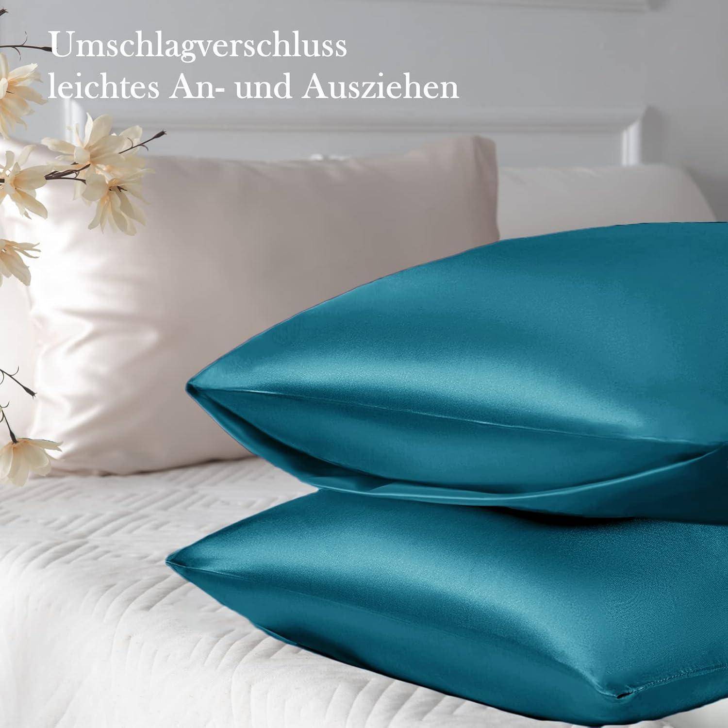 Blaue Satinbezüge auf einem Bett, mit beigen Kissen und Blumen im Hintergrund. Deutscher Text lautet: 