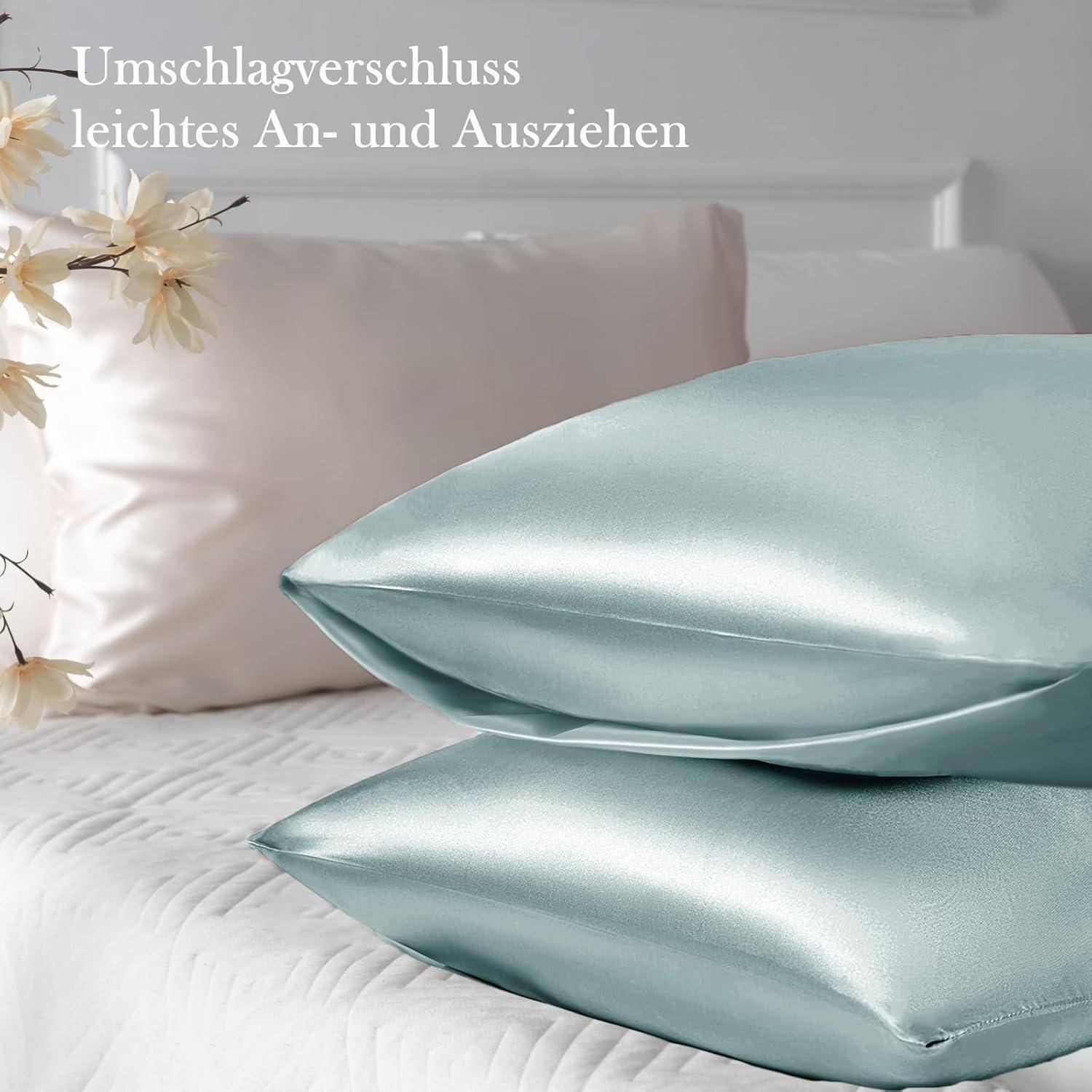 Zwei Satin-Kissenbezüge in einem sanften Blauton sind auf einem Bett gestapelt, mit weißen Wänden und zarten Blumen im Hintergrund, was Luxus und Eleganz vermittelt.