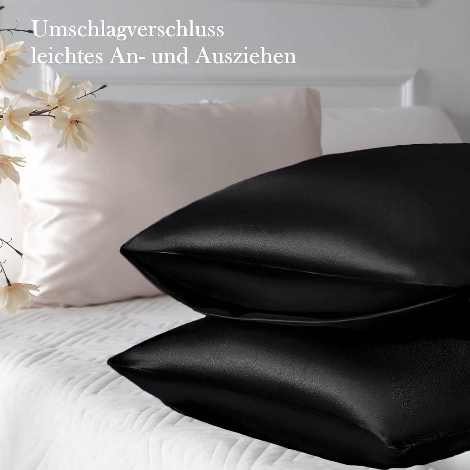 Schwarzer Satin-Kissenbezug auf dem Bett, neben cremefarbenen Kissen und Blumen. Text auf Deutsch lautet: 'Umschlagverschluss leichtes An- und Ausziehen'.