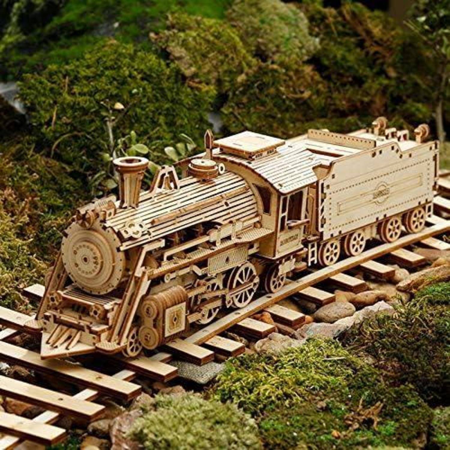 Ein detailliertes Holzmodell eines Zuges steht auf Schienen, umgeben von üppigem grünem Moos, was kunstvolles Handwerk und natürliche Elemente veranschaulicht.