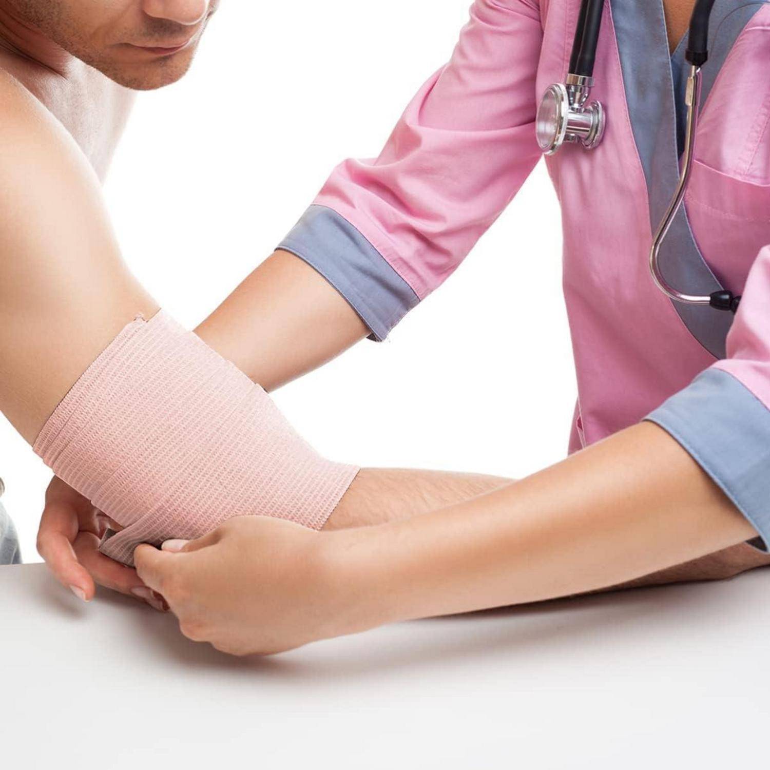 Ein Gesundheitsfachkraft in einer rosa Uniform wickelt einen Verband um den Unterarm einer Person und konzentriert sich darauf, Pflege und Unterstützung zu leisten.
