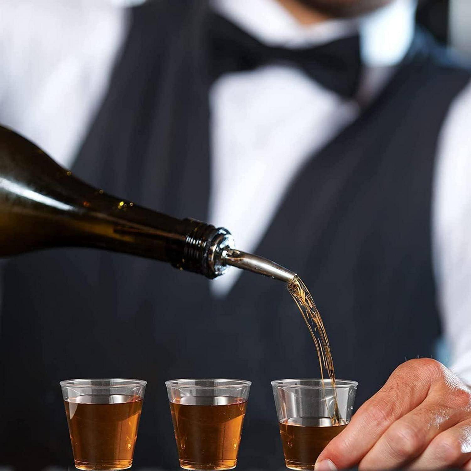 Eine Person gießt Whiskey aus einer Flasche in Schnapsgläser auf einem Tisch. Der Fokus liegt auf der Gießbewegung und den gefüllten Gläsern.