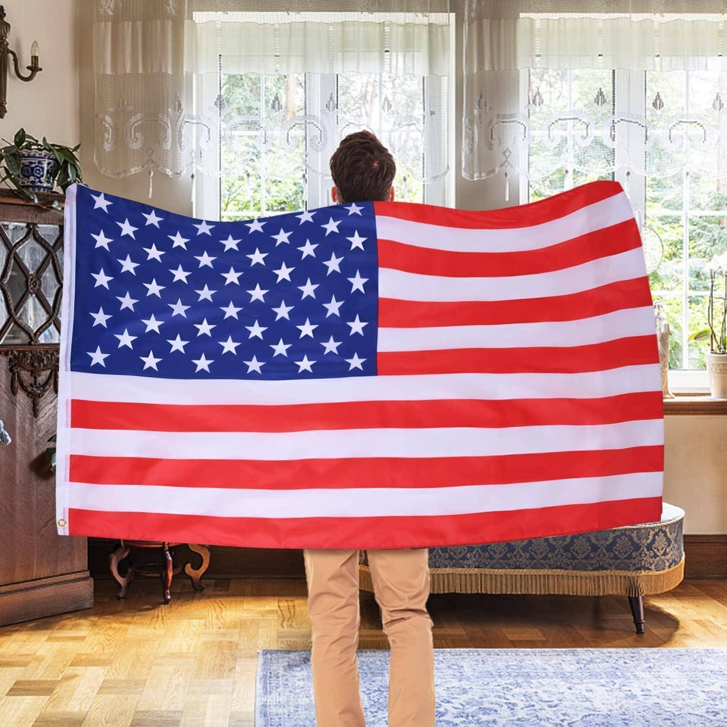 Eine Person steht drinnen und hält eine große Flagge der Vereinigten Staaten, während Sonnenlicht durch ein Fenster im Hintergrund hereinströmt.