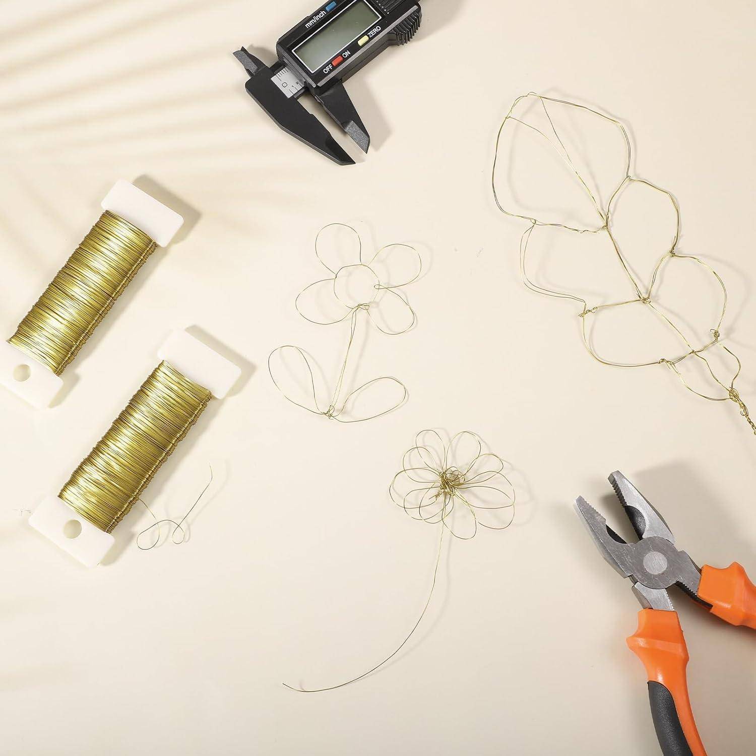 Drahthandwerkswerkzeuge und -materialien, einschließlich Spulen mit Golddraht, Zangen und Drahtblumen, sind auf einer hellen Oberfläche ausgelegt.