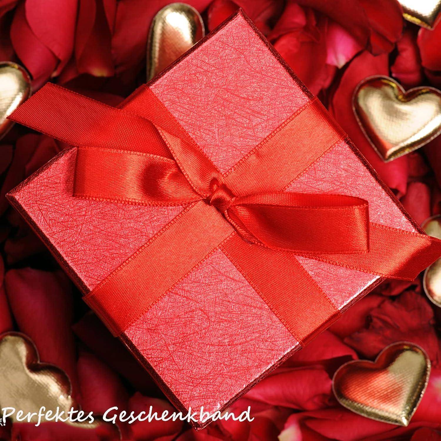 Eine rote Geschenkbox mit einer Schleife liegt auf roten Rosenblütenblättern und goldenen herzförmigen Schokoladen. Text lautet: 