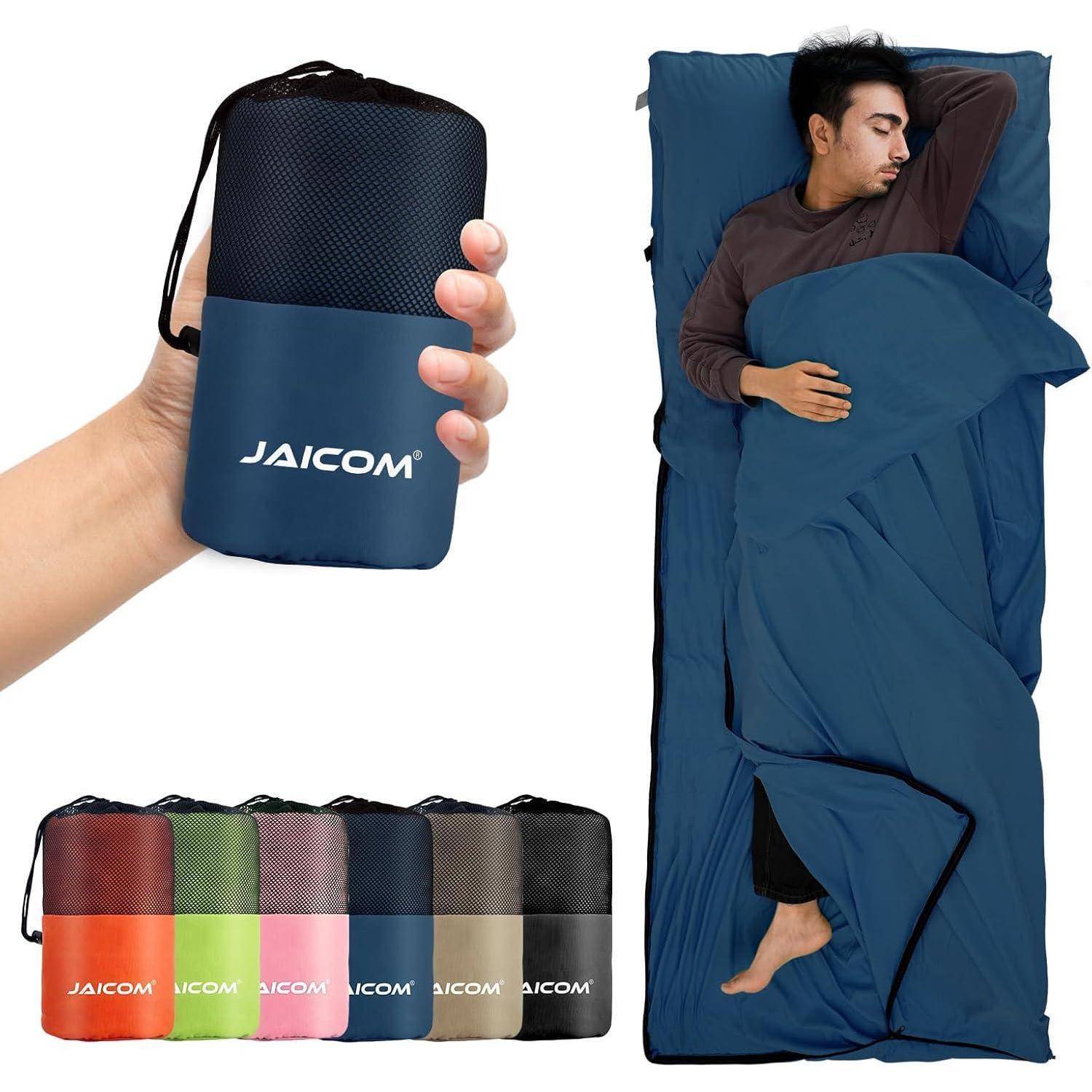Ein Mann schläft in einem blauen Schlafsack. Das Bild zeigt verschiedene zusammengerollte Schlafsäcke in unterschiedlichen Farben und eine Hand, die einen mit 