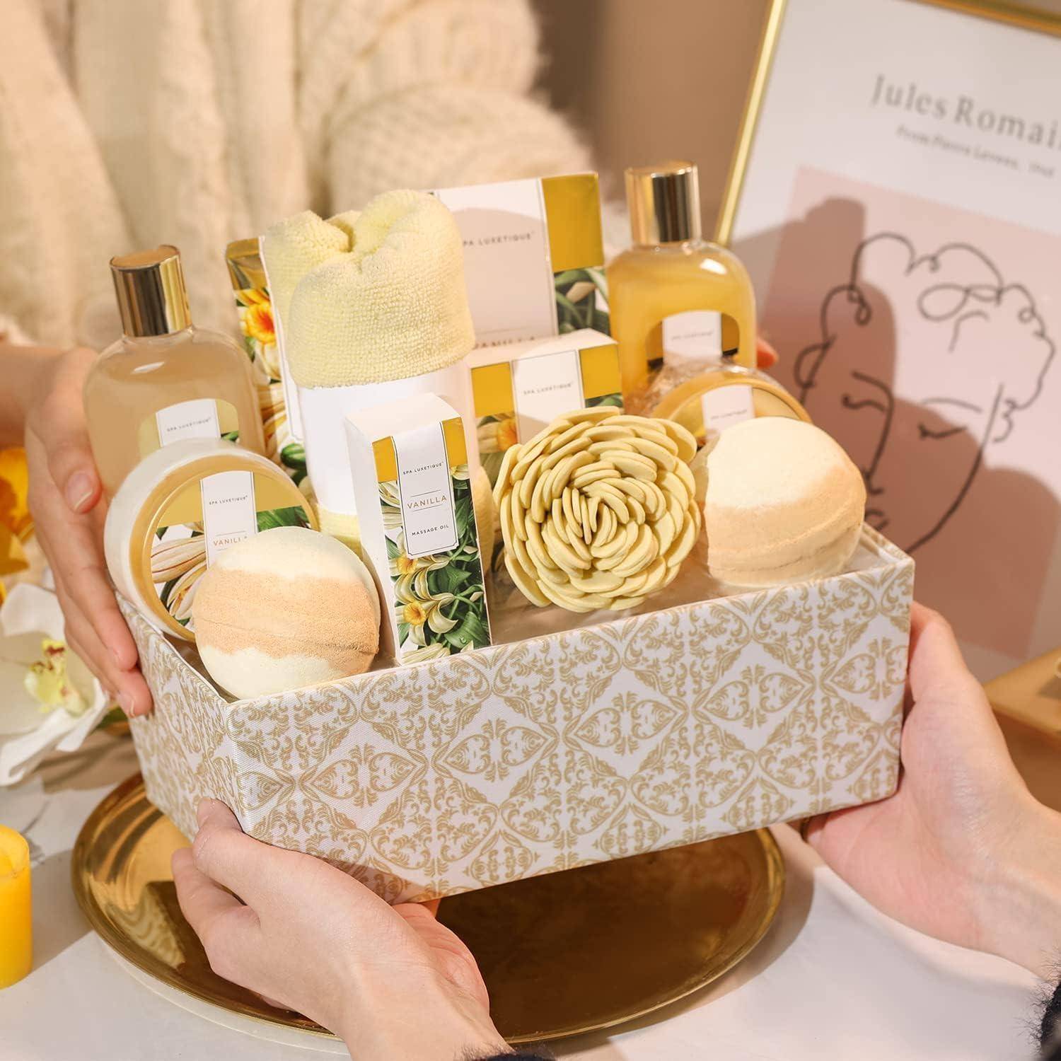 Ein Geschenkkorb mit Badeprodukten, einem Handtuch, einer Blume und Kerzen wird von einer Person an eine andere übergeben und auf einem dekorierten Tisch platziert.
