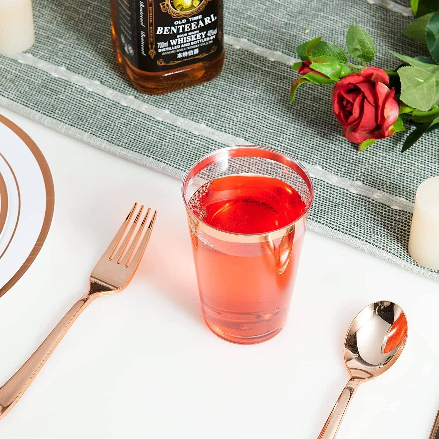 Ein Glas mit rotem Getränk auf einem Esstisch, daneben eine Whiskey-Flasche, eine rote Rose und goldene Bestecke.