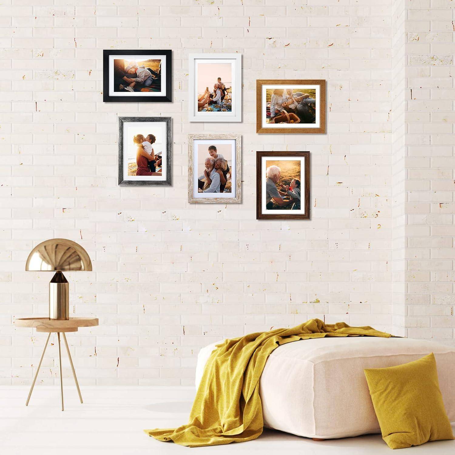 Ein gemütliches Zimmer mit einer weißen Ziegelwand, an der sechs gerahmte Familienfotos hängen. Eine moderne Lampe und ein großer beiger Hocker mit einer gelben Decke befinden sich in der Nähe.