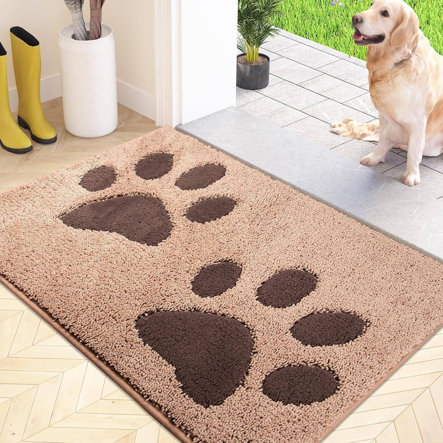 Eine beige Fußmatte mit großen braunen Pfotenabdrücken liegt auf dem Boden. Ein Hund sitzt auf einer gefliesten Fläche neben der Fußmatte, nahe einer grünen Pflanze.