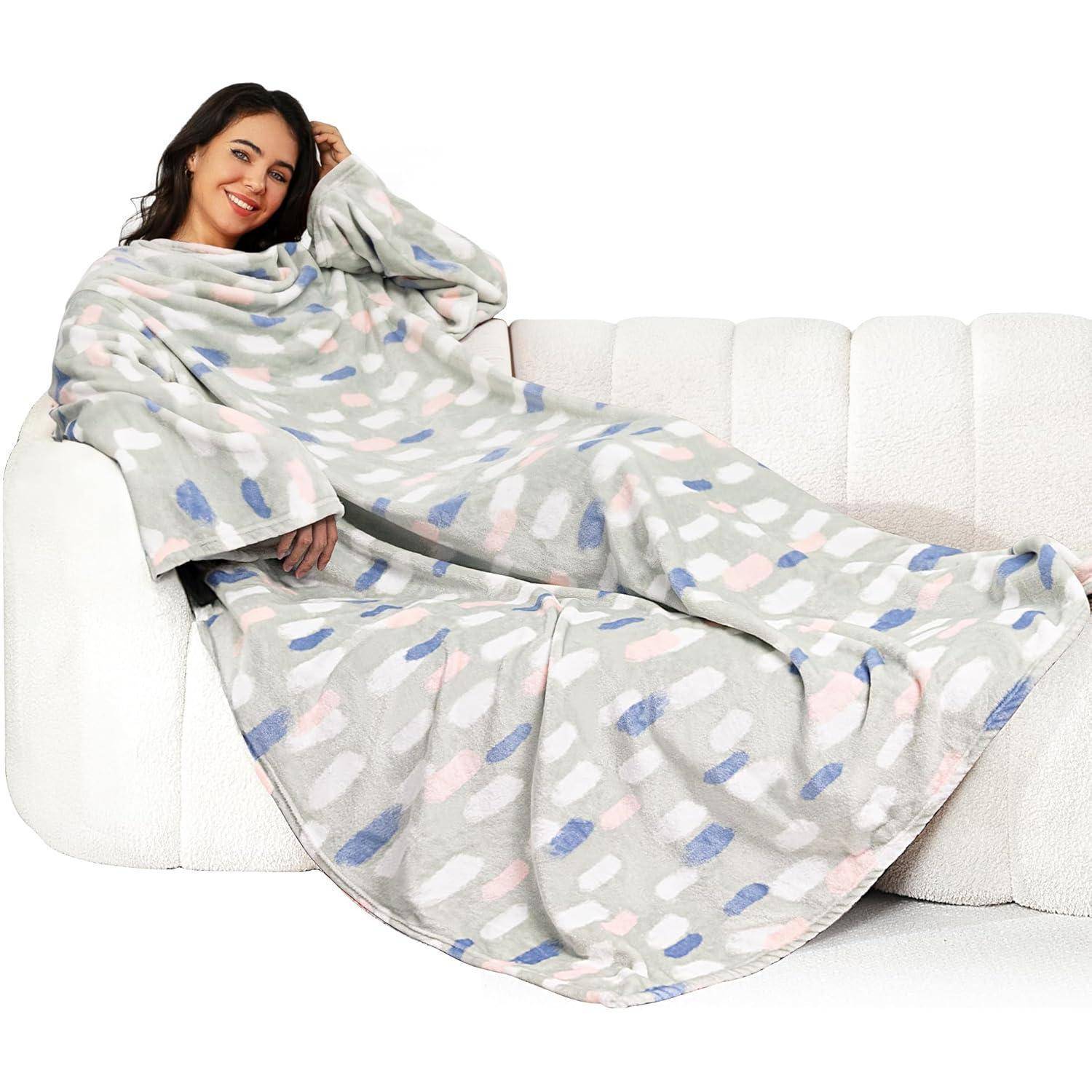 Eine Person, die eine gemütliche, gemusterte Kuscheldecke mit Ärmeln trägt, sitzt bequem auf einem weißen Sofa und lächelt, wobei sie Wärme und Entspannung ausstrahlt.