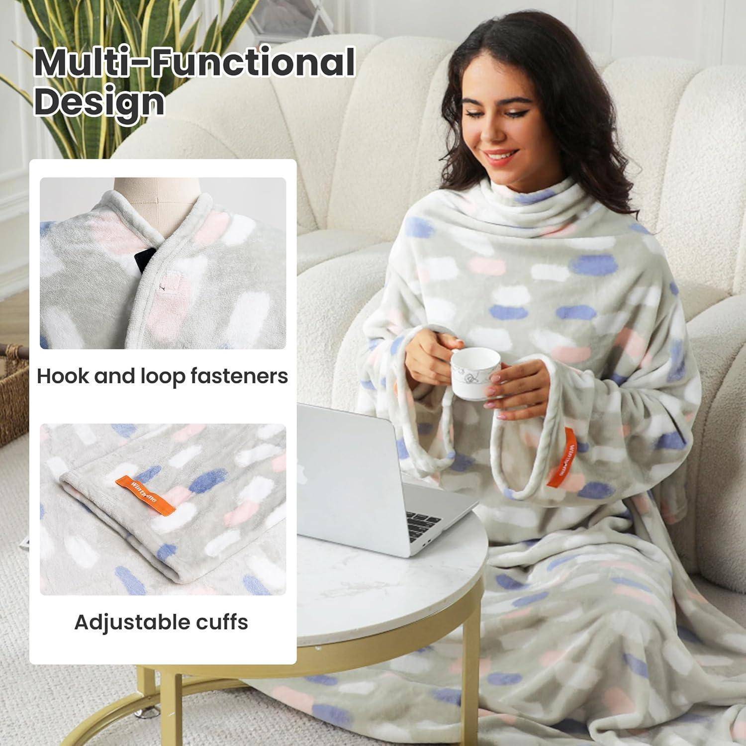 Frau in gemusterter Decke mit verstellbaren Manschetten und Hakenverschlüssen, auf einem Sofa sitzend, eine Tasse haltend, mit einem Laptop auf dem Tisch.