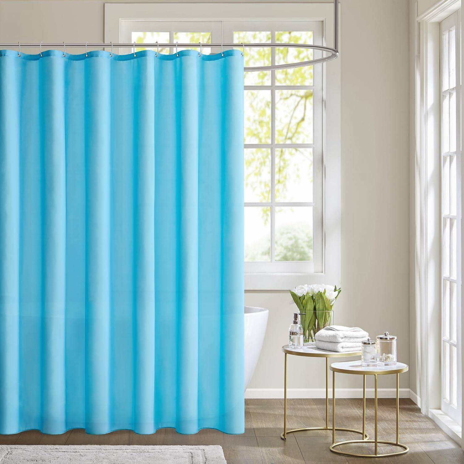 Ein Badezimmer mit einem blauen Duschvorhang, einem Fenster, das Tageslicht hereinlässt, und einem kleinen runden Tisch mit einem Getränk und Handtüchern in der Nähe.