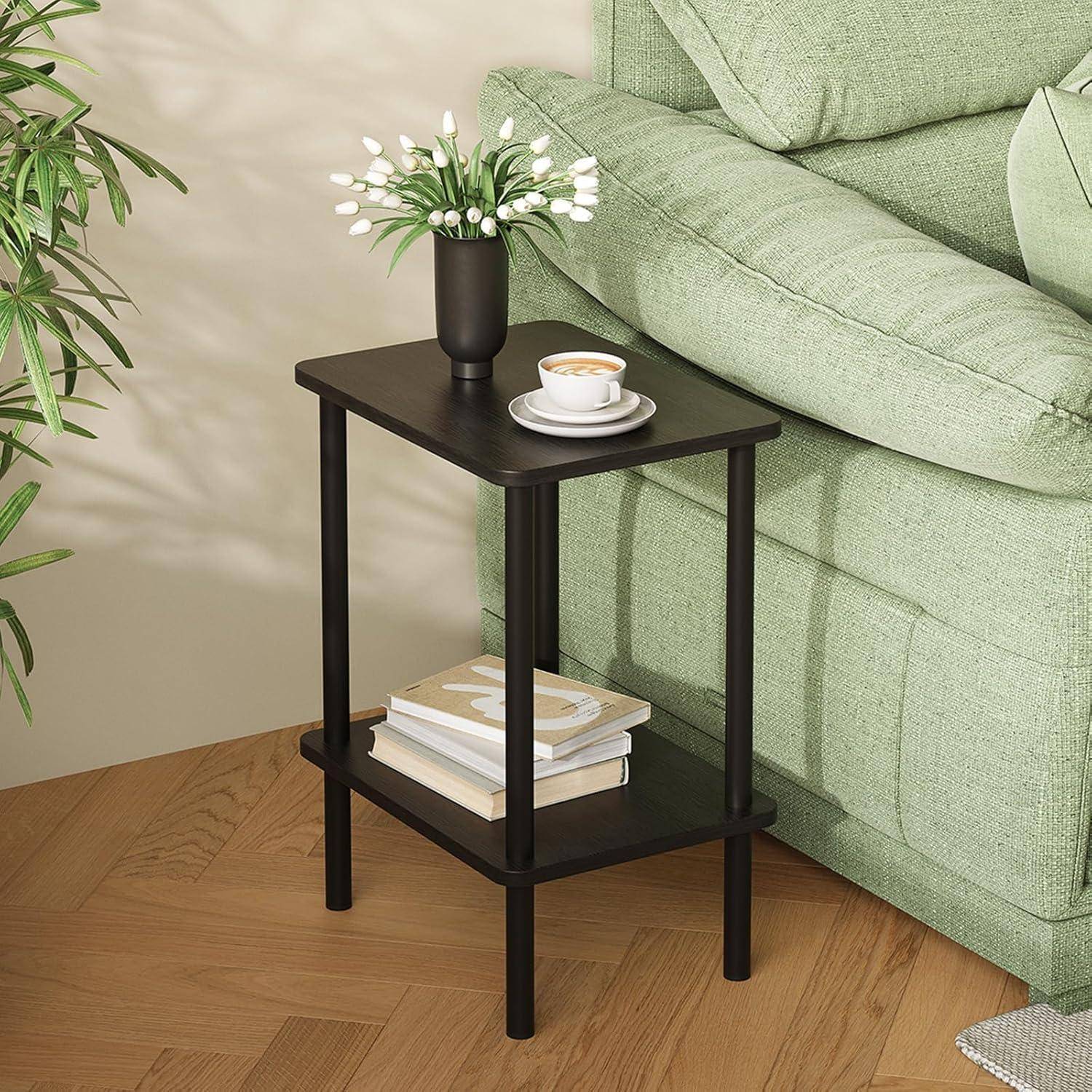 Ein kleiner schwarzer Beistelltisch neben einem grünen Sofa trägt eine Topfpflanze, eine Kaffeetasse und gestapelte Bücher und schafft eine gemütliche Wohnzimmeratmosphäre.