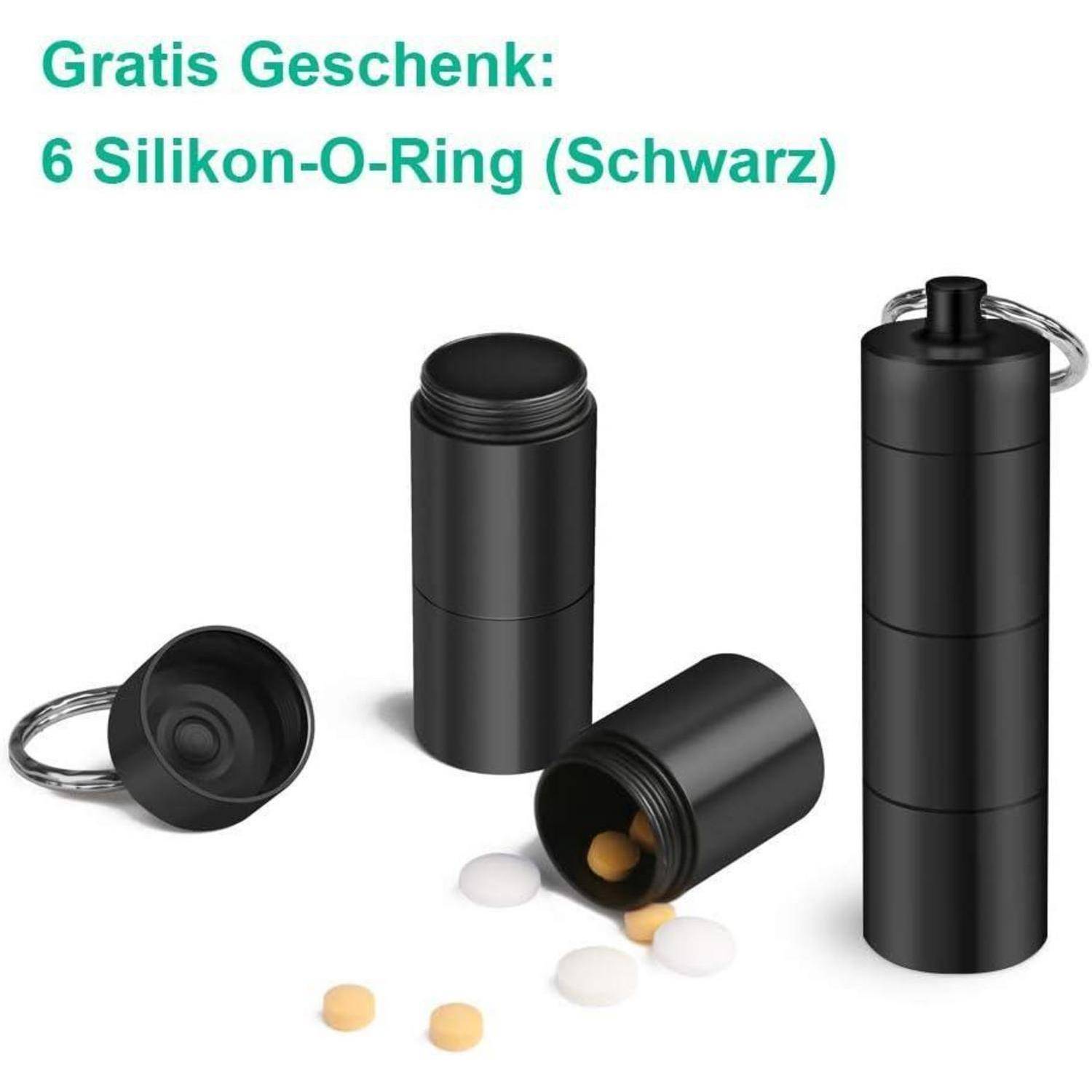 Ein schwarzer Pillenetui-Schlüsselanhänger wird geöffnet mit kleinen Pillen, die herausfallen. Text lautet: 'Gratis Geschenk: 6 Silikon-O-Ringe (Schwarz)'.