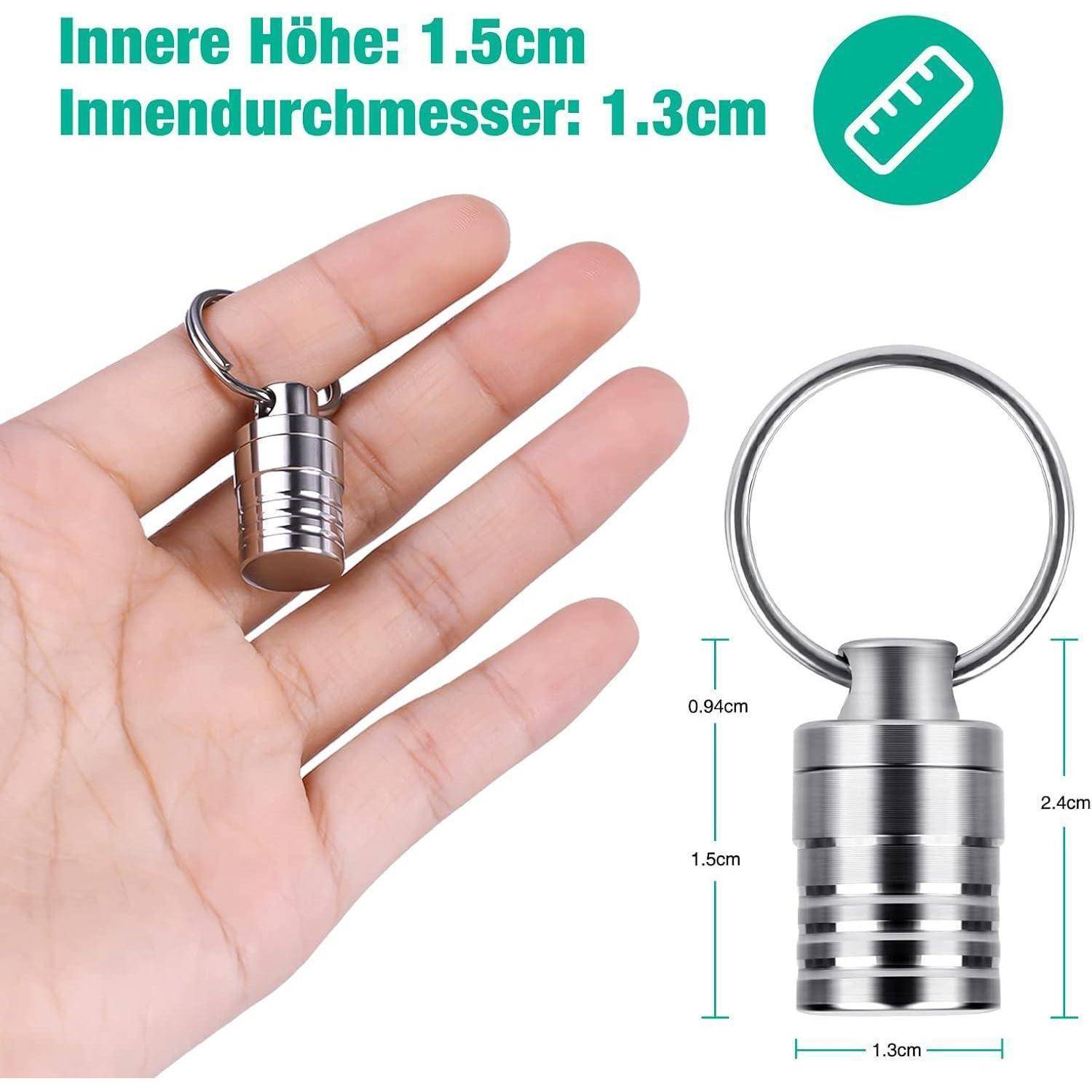 Eine Hand hält eine kleine, zylindrische Metallkapsel mit einem Schlüsselring. Maße sind angegeben: Höhe 1,5 cm, Innendurchmesser 1,3 cm.