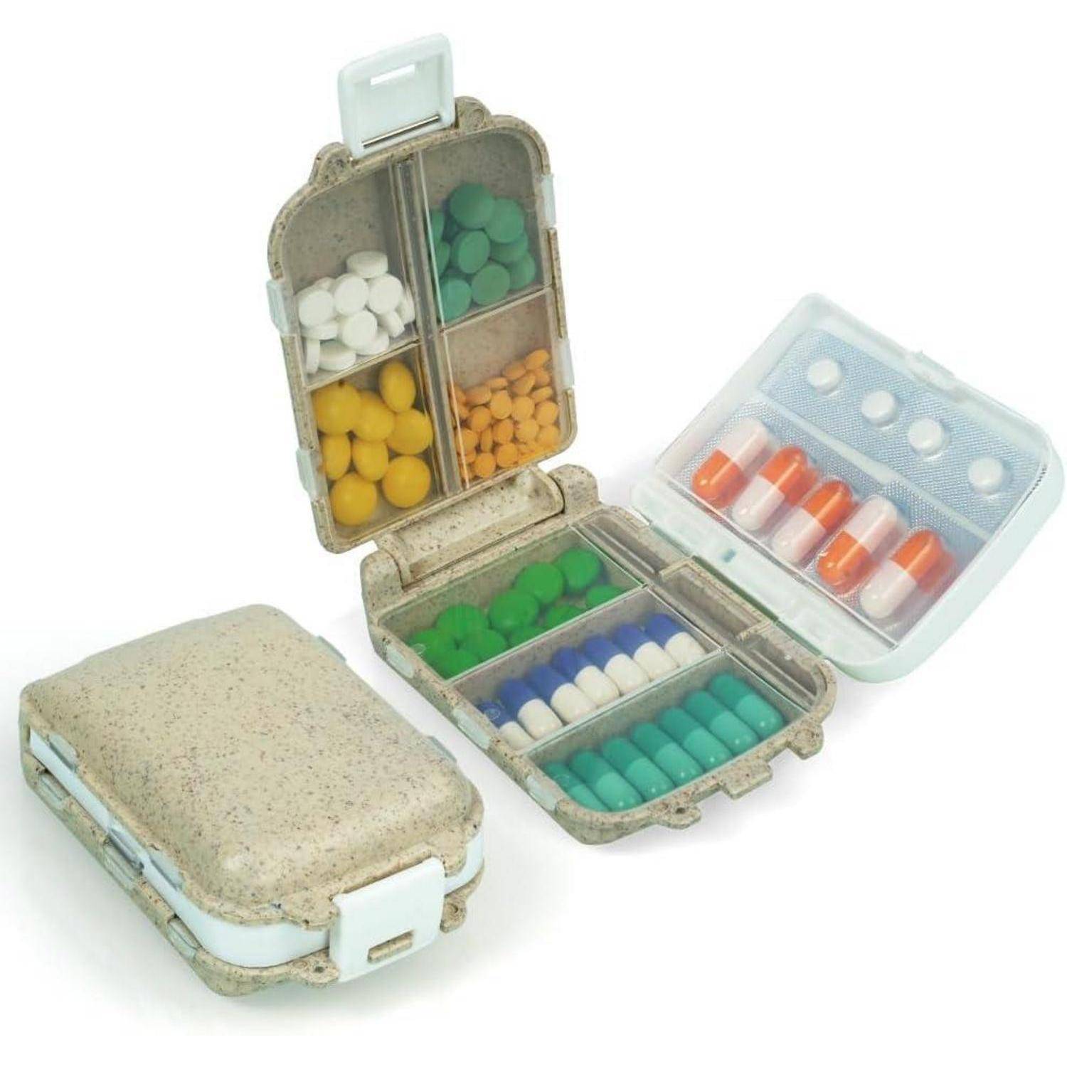 Eine kleine, tragbare Pillenbox ist geöffnet und zeigt verschiedenfarbige Pillen in beschrifteten Fächern, daneben liegt der geschlossene Behälter.