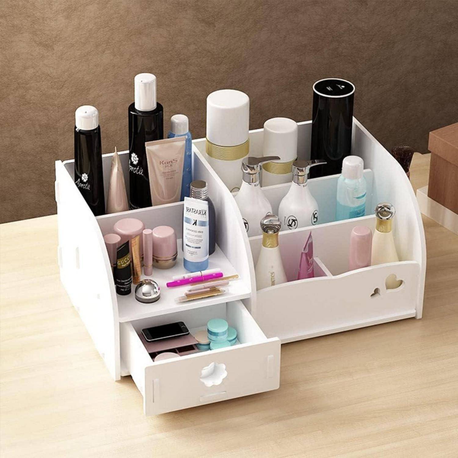 Ein weißer Make-up-Organizer auf einem Holztisch beherbergt verschiedene Beautyprodukten, darunter Flaschen, Lippenstifte und Pinsel. Eine Schublade ist leicht geöffnet und gibt sorgfältig angeordnete Gegenstände preis.