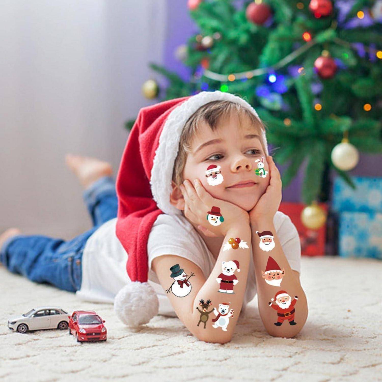 Ein Kind mit einer Weihnachtsmannmütze liegt auf dem Boden, im Hintergrund ein Weihnachtsbaum, umgeben von festlichen Spielsachen und Dekorationen.