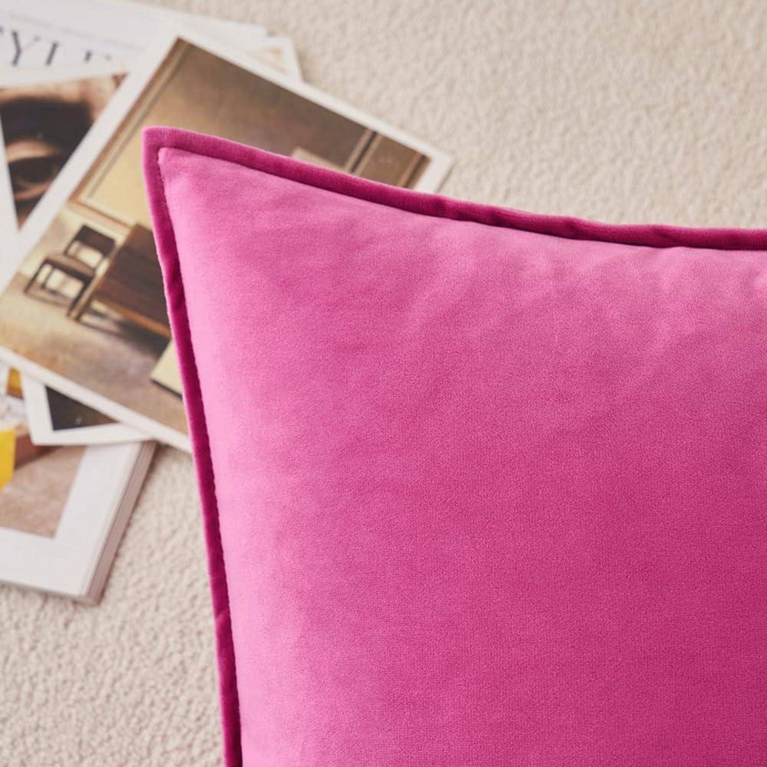 Ein leuchtend pinker Kissen auf einem beigen Teppich, wobei Zeitschriften im Hintergrund leicht zu erkennen sind.