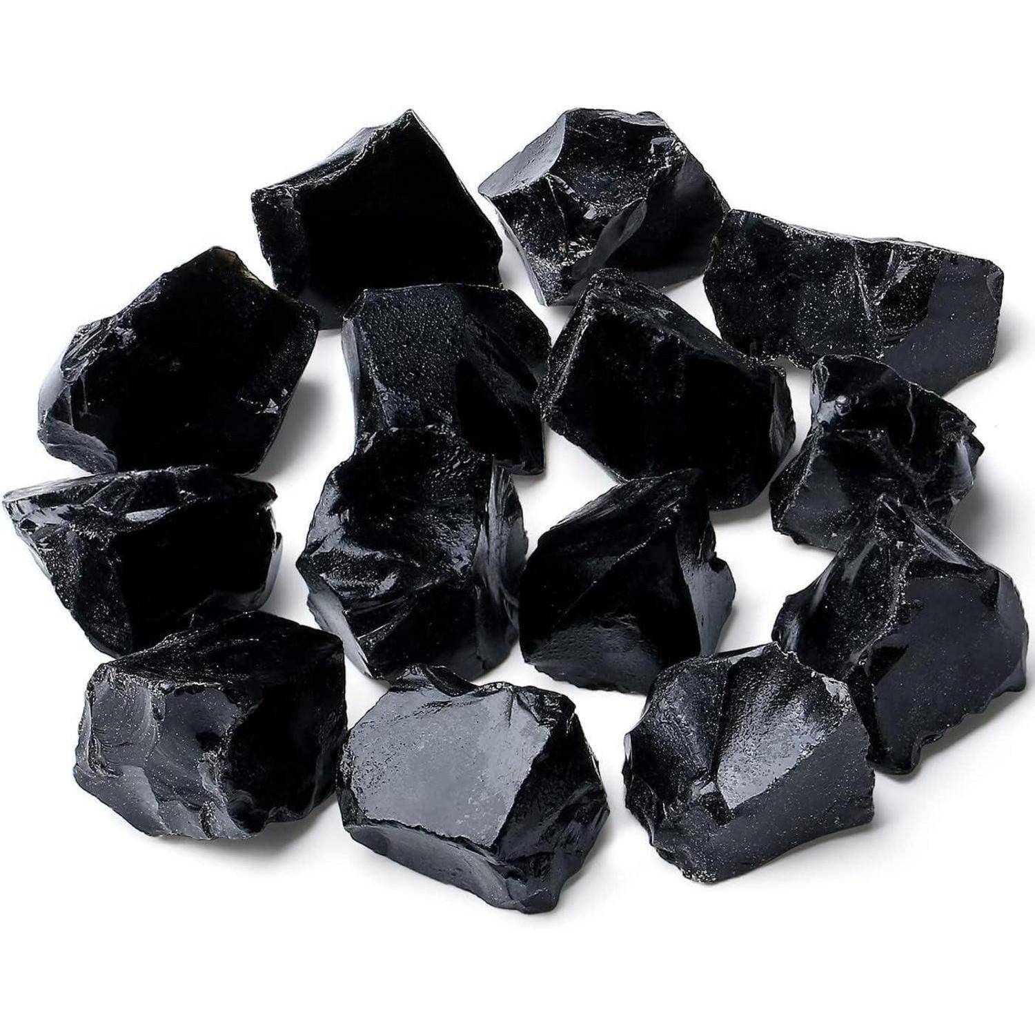 Glänzende schwarze Obsidiansteine, die auf einer weißen Oberfläche angeordnet sind und ihre unregelmäßigen Formen und glatten Texturen zur Geltung bringen.