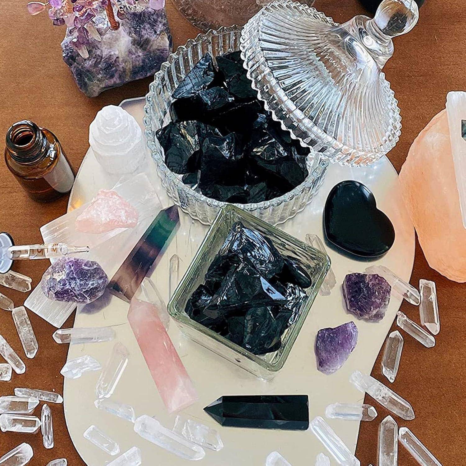 Verschiedene Kristalle wie Obsidian, Amethyst und Rosenquarz, auf einem Tisch mit einem Glasgefäß und dekorativen Elementen angeordnet.