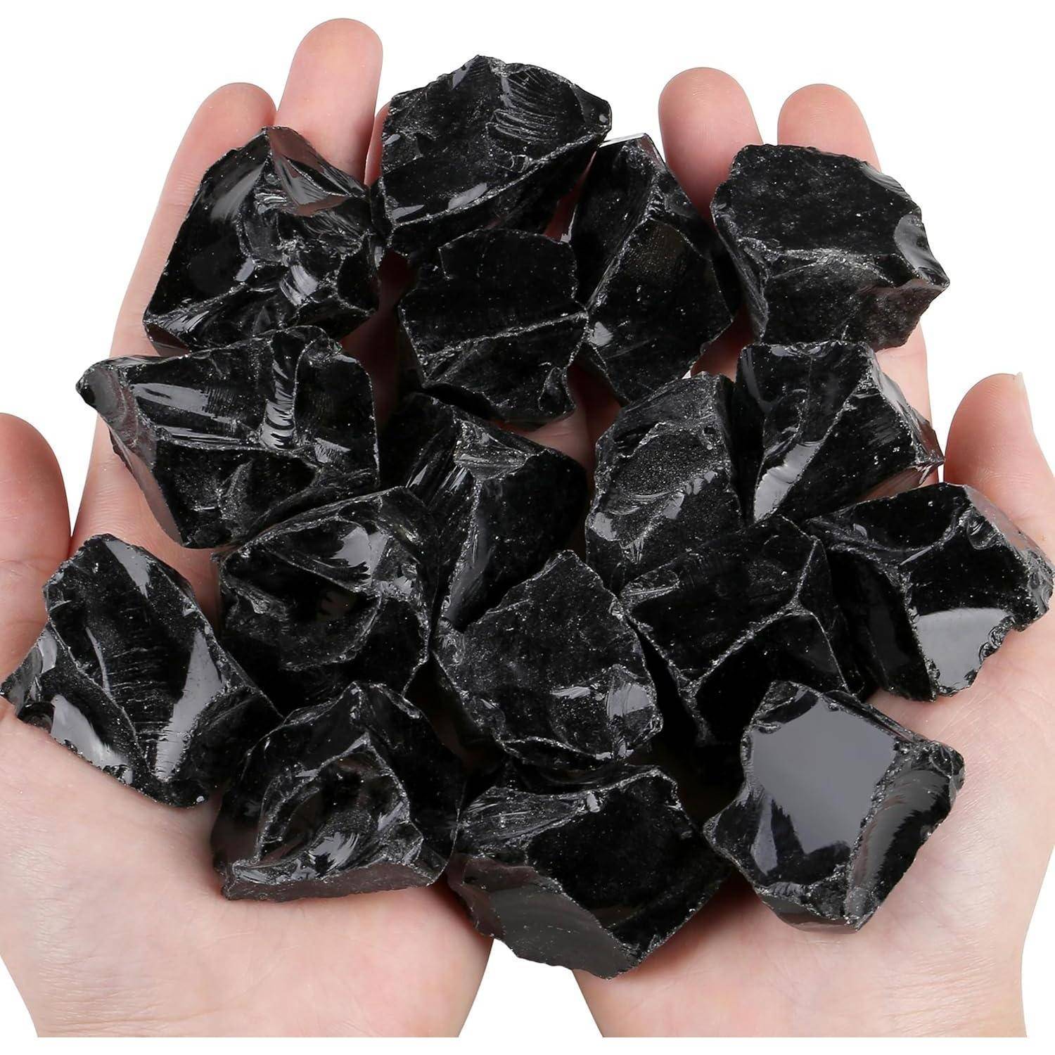 Hände, die mehrere glänzende schwarze Obsidiansteine halten, die das Licht reflektieren und unregelmäßige Formen sowie glatte, glänzende Oberflächen zeigen.