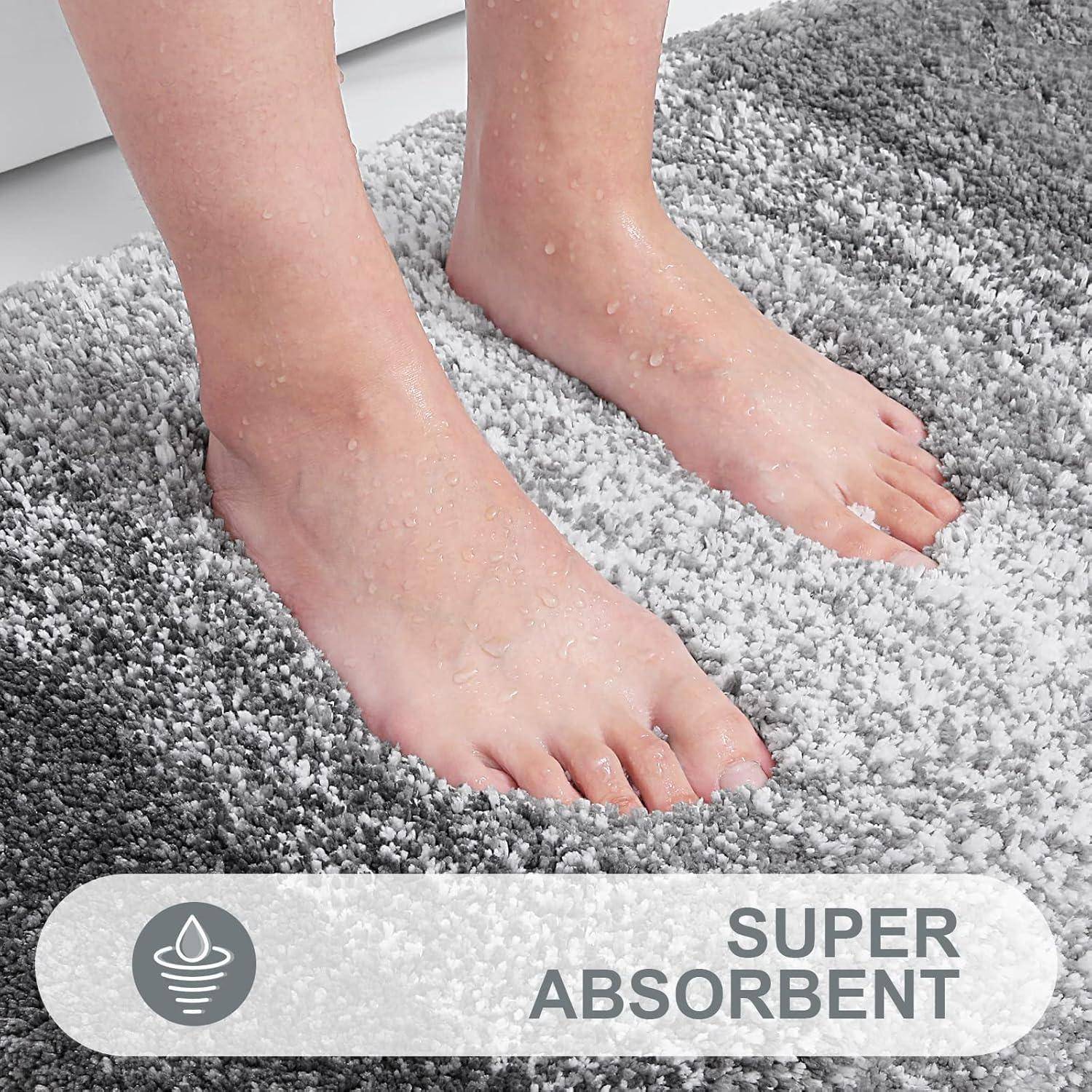 Nackte Füße auf einem zweifarbigen grauen Hochflor-Teppich, der mit ‚Super Absorbierend' gekennzeichnet ist. Das Bild betont die Fähigkeit des Teppichs, Feuchtigkeit aufzunehmen.