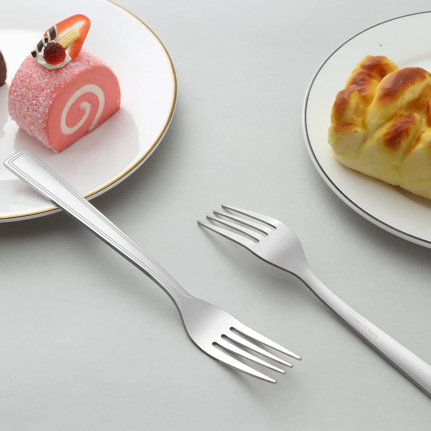 Zwei silberne Gabeln auf einem Tisch neben einem bunten Desserteller mit einer Rolle und einem Gebäckstück.