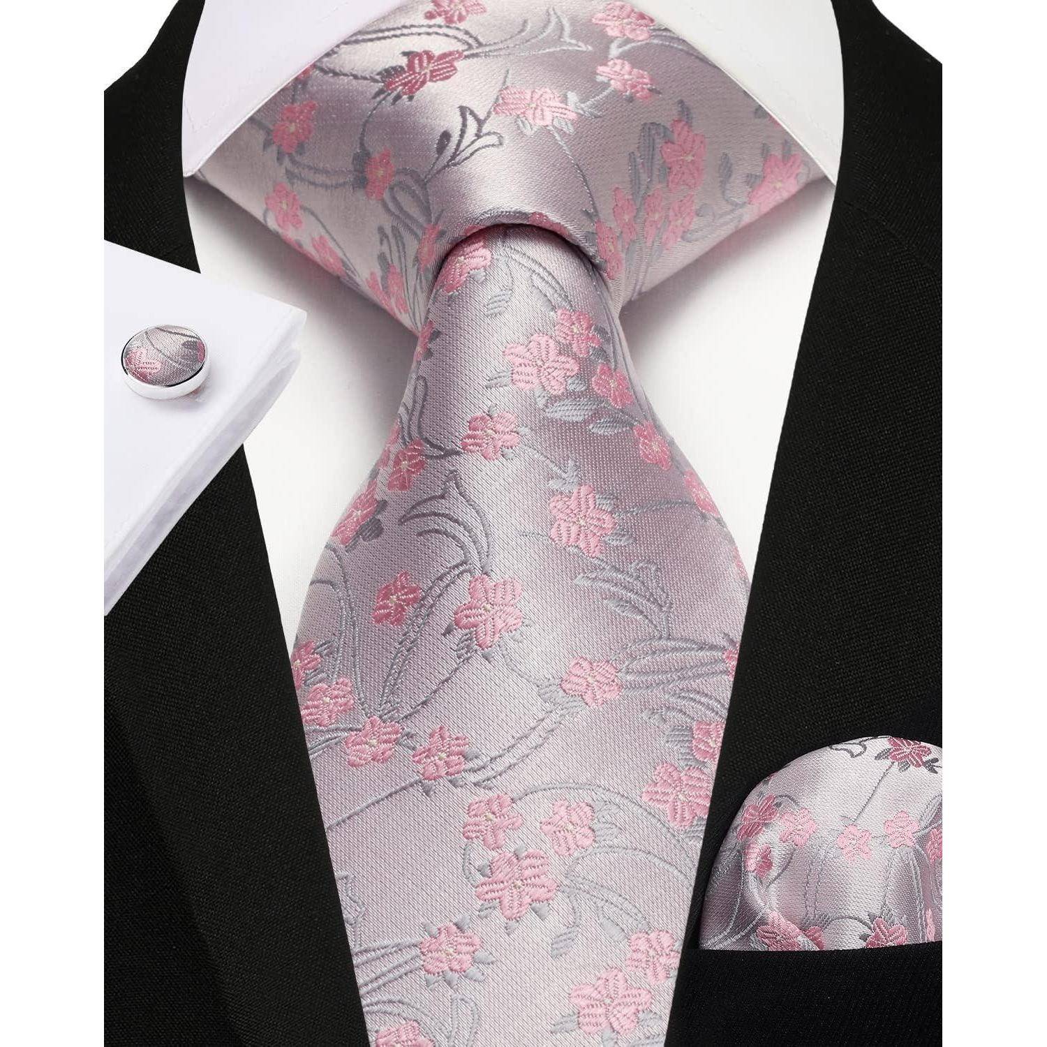 Eine Nahaufnahme eines formellen Outfits mit einer hellgrauen Krawatte mit rosa Blumenmuster, passendem Einstecktuch und weißem Hemd mit Französischen Manschetten.