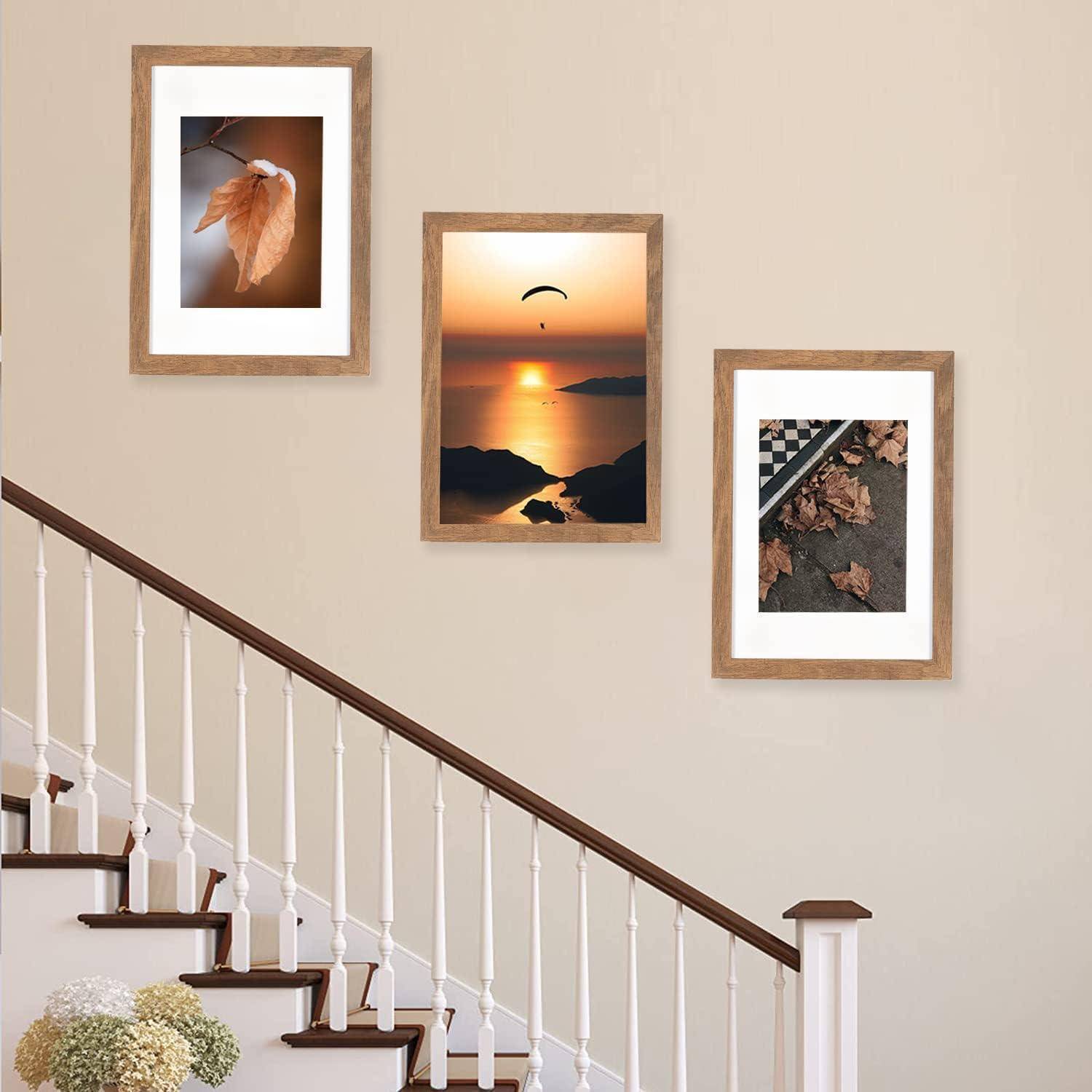 Drei gerahmte Fotografien hängen an einer beigen Wand über einer Treppe. Von links nach rechts: ein Blatt, ein Sonnenuntergang über Wasser und gefallene Blätter auf einem Raster.