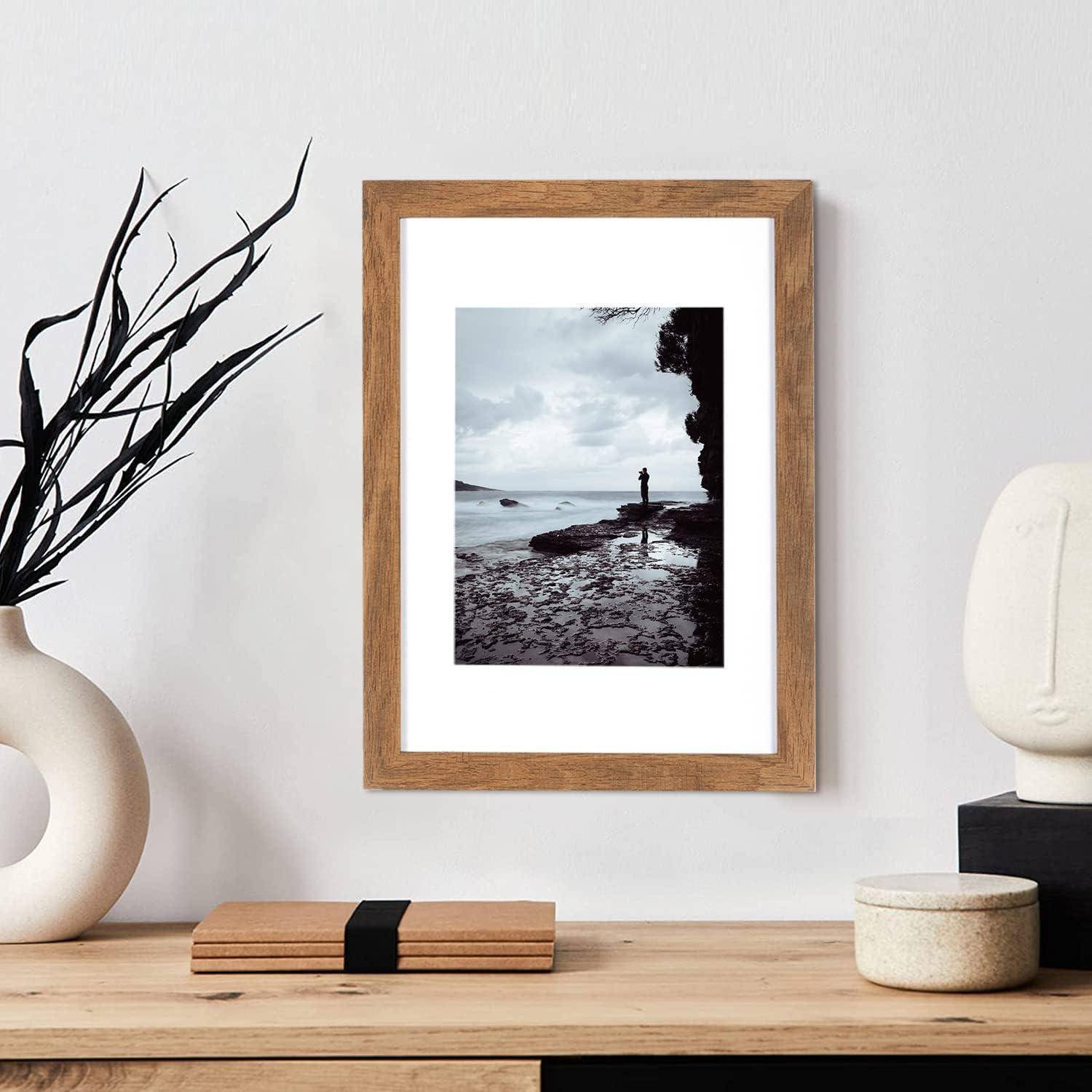 Ein gerahmtes Schwarz-Weiß-Foto einer Person, die am Meer steht, hängt an einer neutral getönten Wand, umgeben von minimalistischer Dekoration.