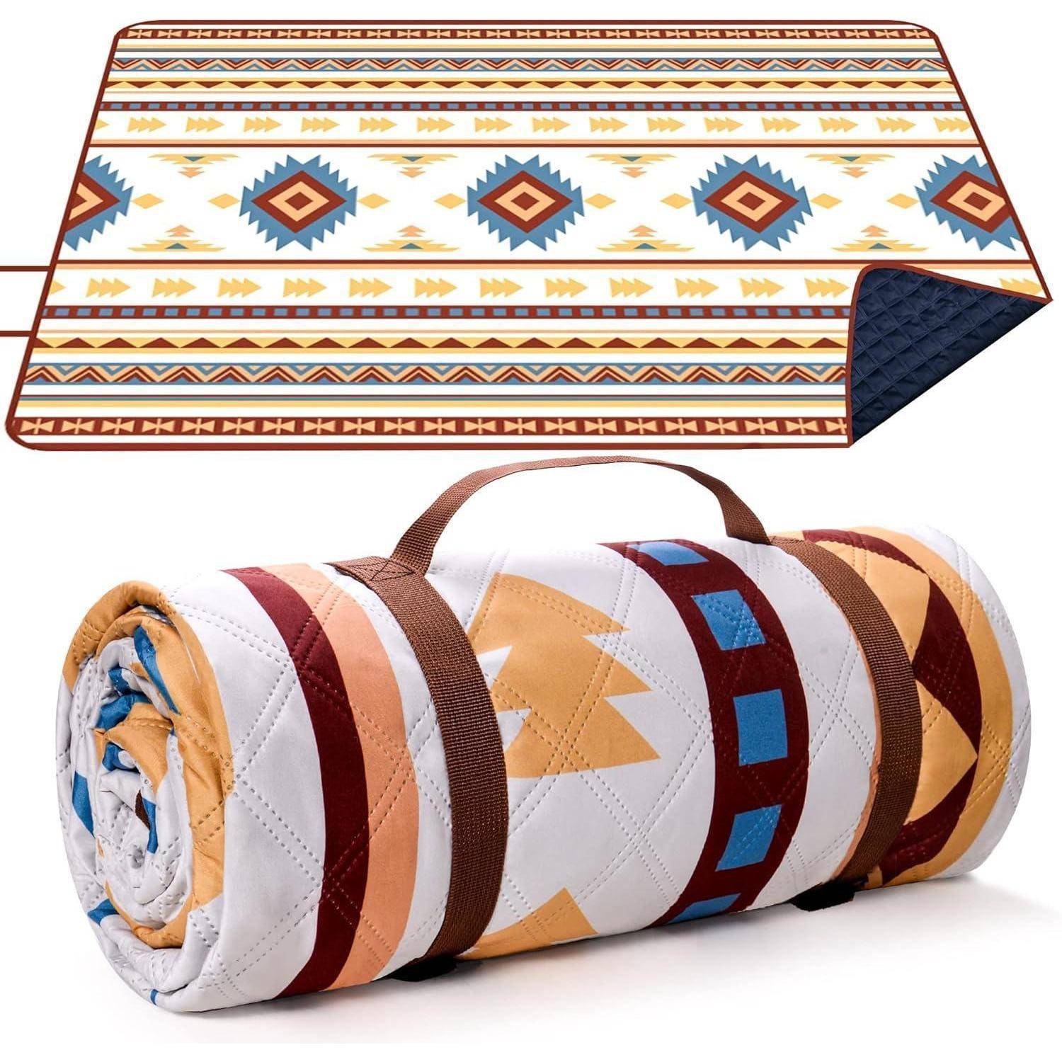Gesteppte Picknickdecke mit geometrischem Muster in Blau, Orange und Weiß, aufgerollt mit einem braunen Trageriemen.