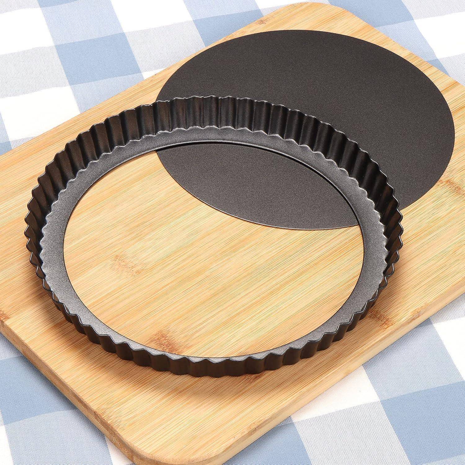 Eine runde Tartform mit herausnehmbarem Boden steht auf einem Holzschneidebrett, das auf einer blau-weiß karierter Tischdecke liegt.