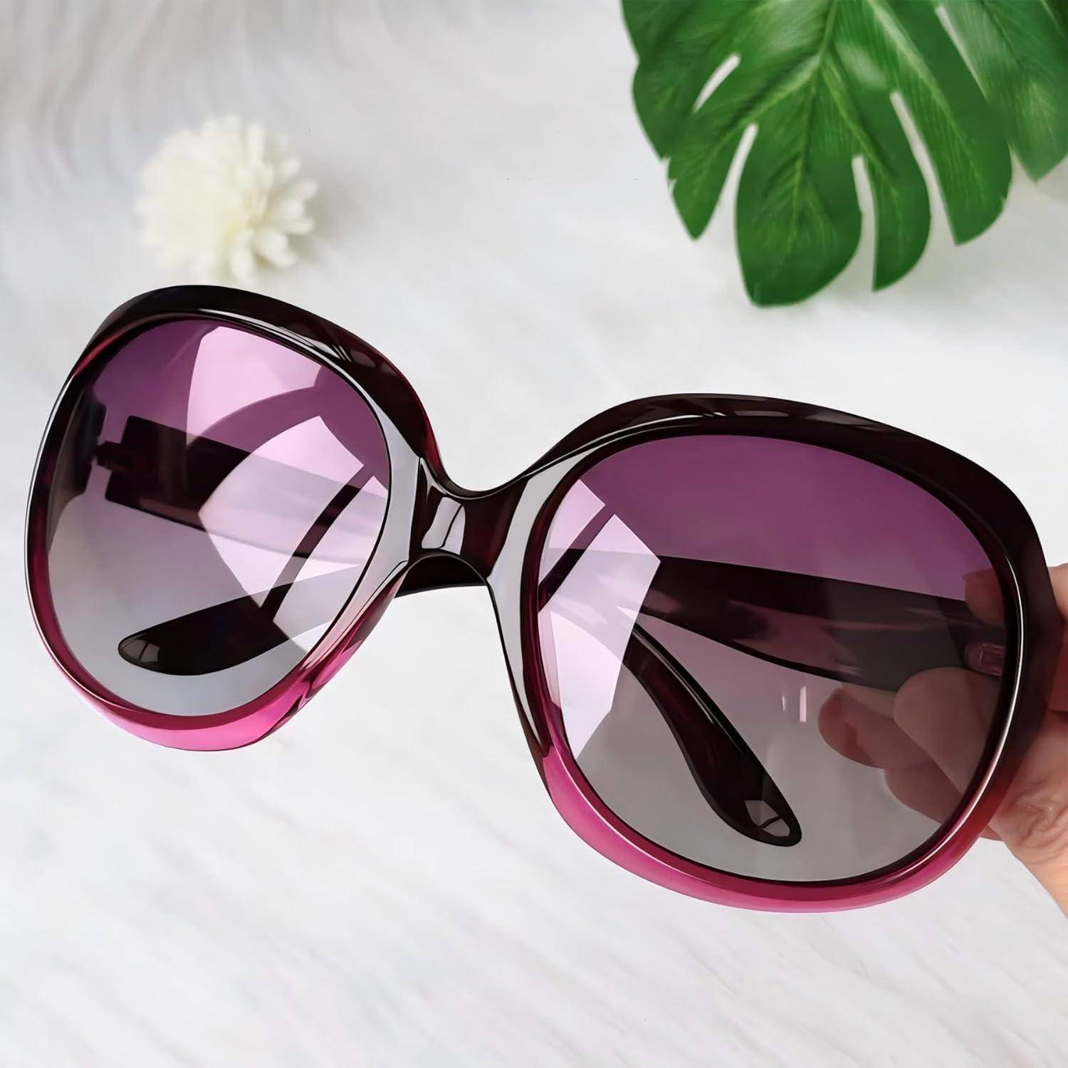 Ein Paar überdimensionale, lila getönte Sonnenbrille, vor einem weißen Hintergrund gehalten, mit einem grünen Blatt und einer kleinen cremefarbenen Blüte in der Nähe.