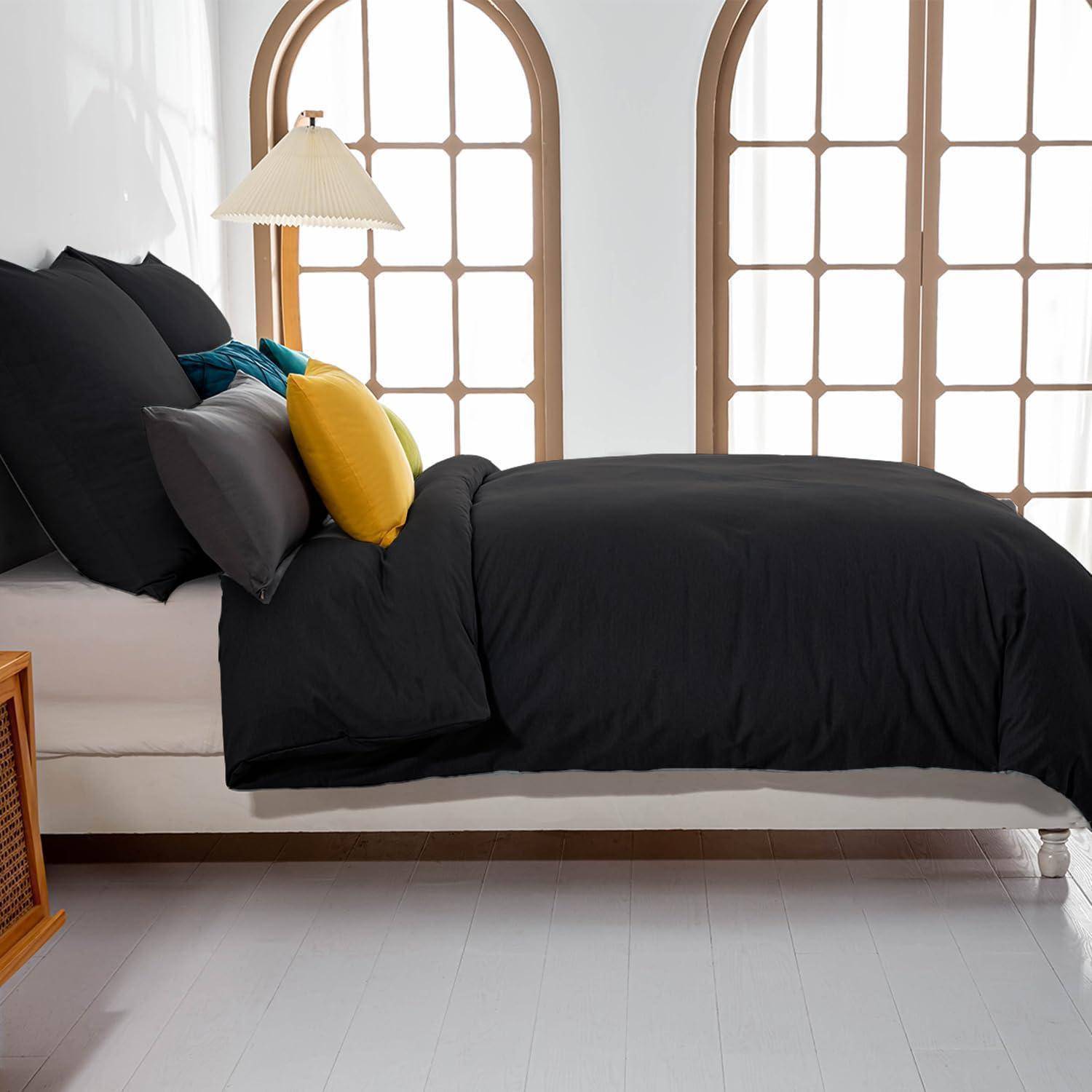 Ein Schlafzimmer mit einem ordentlich gemachten Bett, das mit schwarzer Bettwäsche und verschiedenen Kissen ausgestattet ist. Ein Holznachttisch mit einer Lampe steht neben Bogenfenstern.