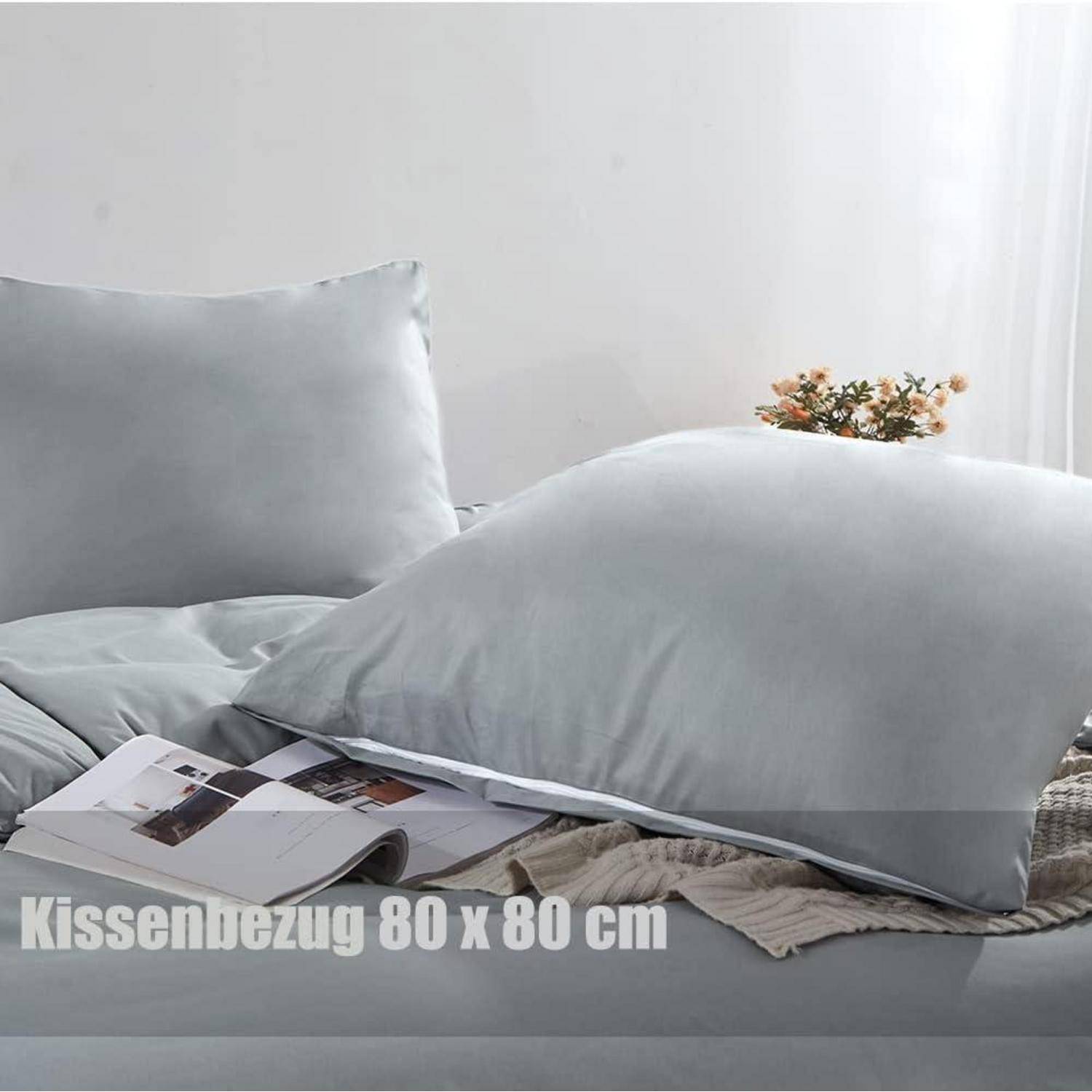 Zwei große graue Kissen auf einem Bett mit einer Zeitschrift in der Nähe. Text lautet 