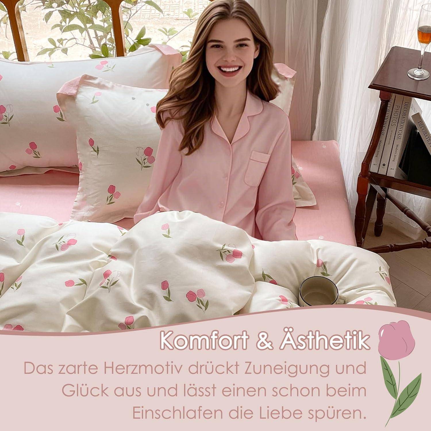 Eine Person in rosa Pyjamas lächelt auf einem Bett mit blumenmustrigen Laken. Eine Rose in einer Vase steht auf dem nahe gelegenen Nachttisch.