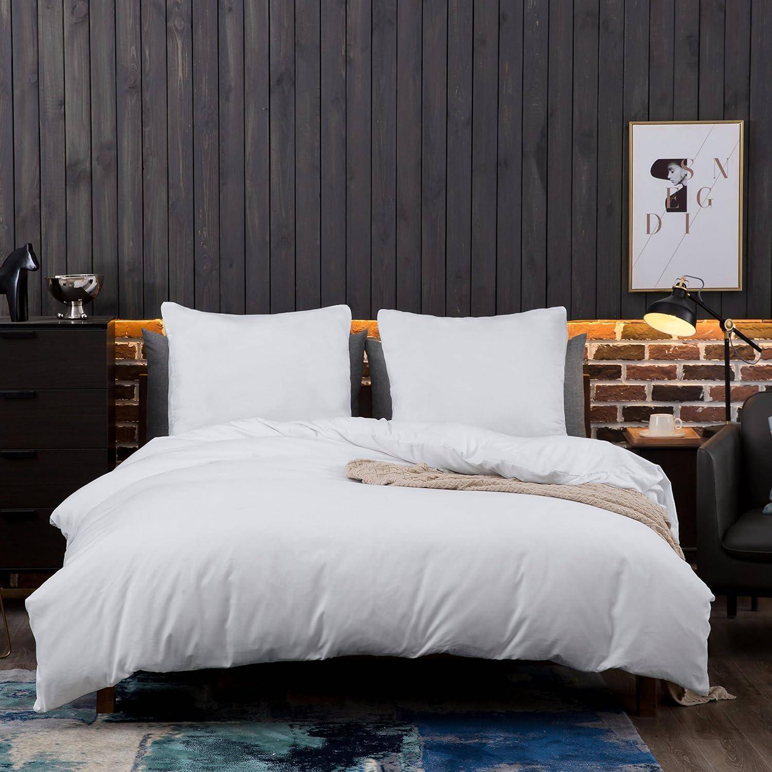 Ein gemütliches Schlafzimmer zeigt ein Bett mit weißer Bettwäsche, einem grauen gepolsterten Kopfteil und dekorativen Kissen, vor einer Holzakzentwand.