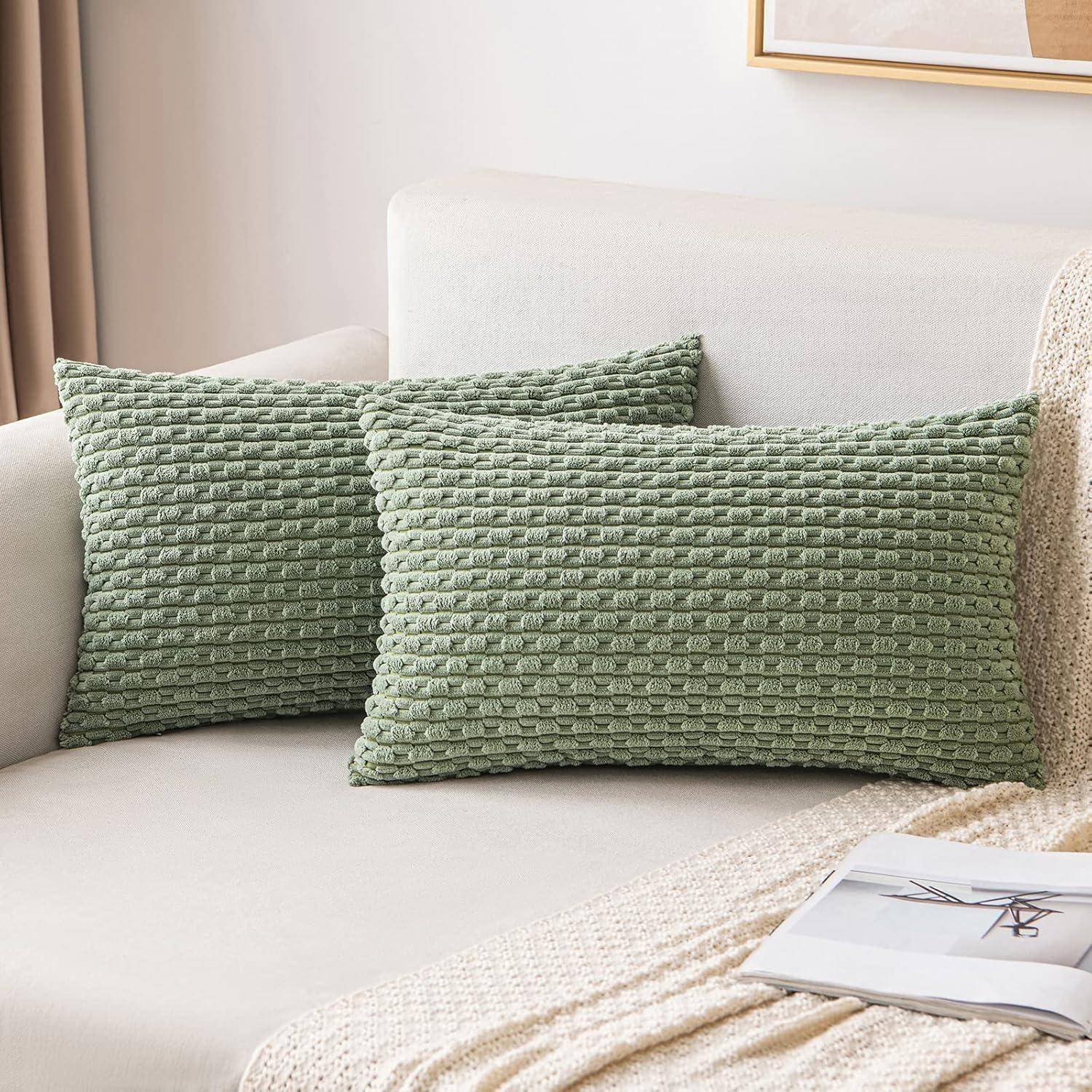 Zwei strukturierte grüne Kissen auf einem beigen Sofa mit einer zusammengelegten weißen Decke und einer Zeitschrift in der Nähe, wodurch eine gemütliche Wohnzimmeratmosphäre entsteht.