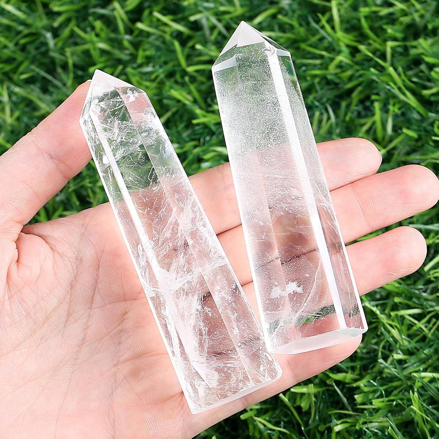 Eine Hand, die zwei durchsichtige Bergkristallspitzen hält, jeweils mit einer spitzen Endung, vor einem Hintergrund aus grünem Gras.