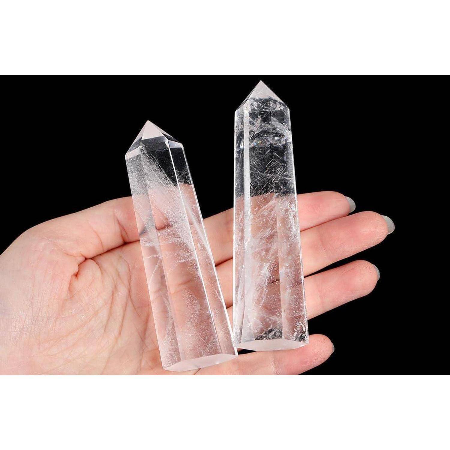 Eine Hand hält zwei durchsichtige Bergkristall-Türme vor einem schwarzen Hintergrund und zeigt dabei ihre transparenten und reflektierenden Eigenschaften.