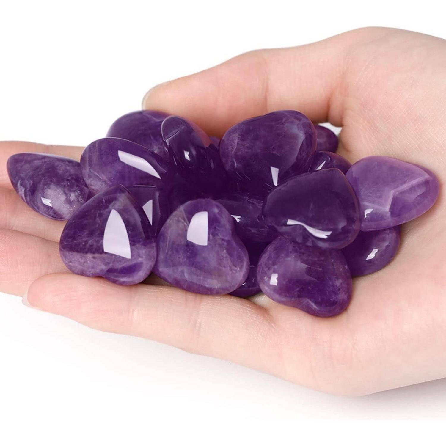 Eine Hand, die mehrere polierte Amethyststeine hält und deren glatte Textur und reiche, lebendige Farbe zeigt.