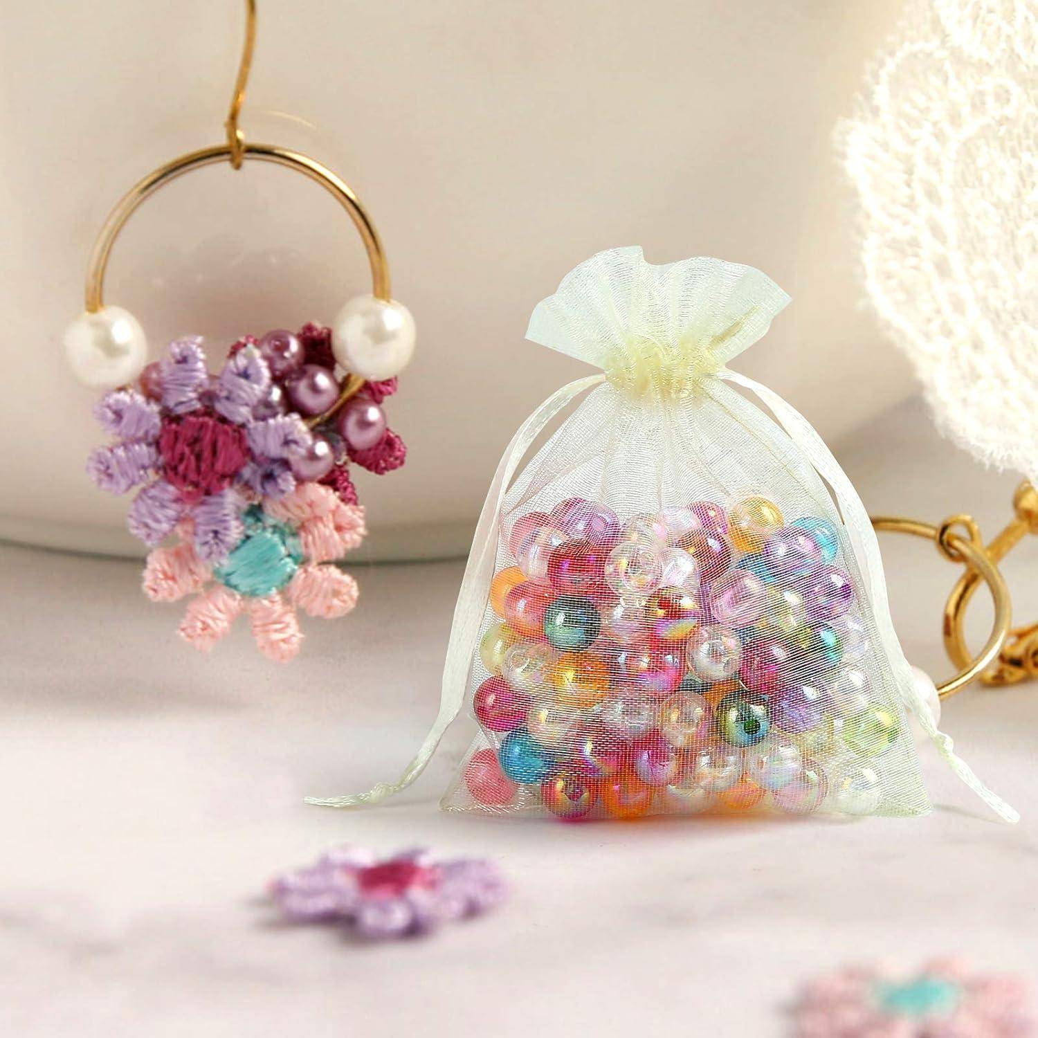 Eine kleine, durchsichtige Tasche gefüllt mit bunten Perlen liegt auf einer Oberfläche neben einem Blumenohrringe. Beide Gegenstände zeigen lebendige Farbtöne und filigrane Details.