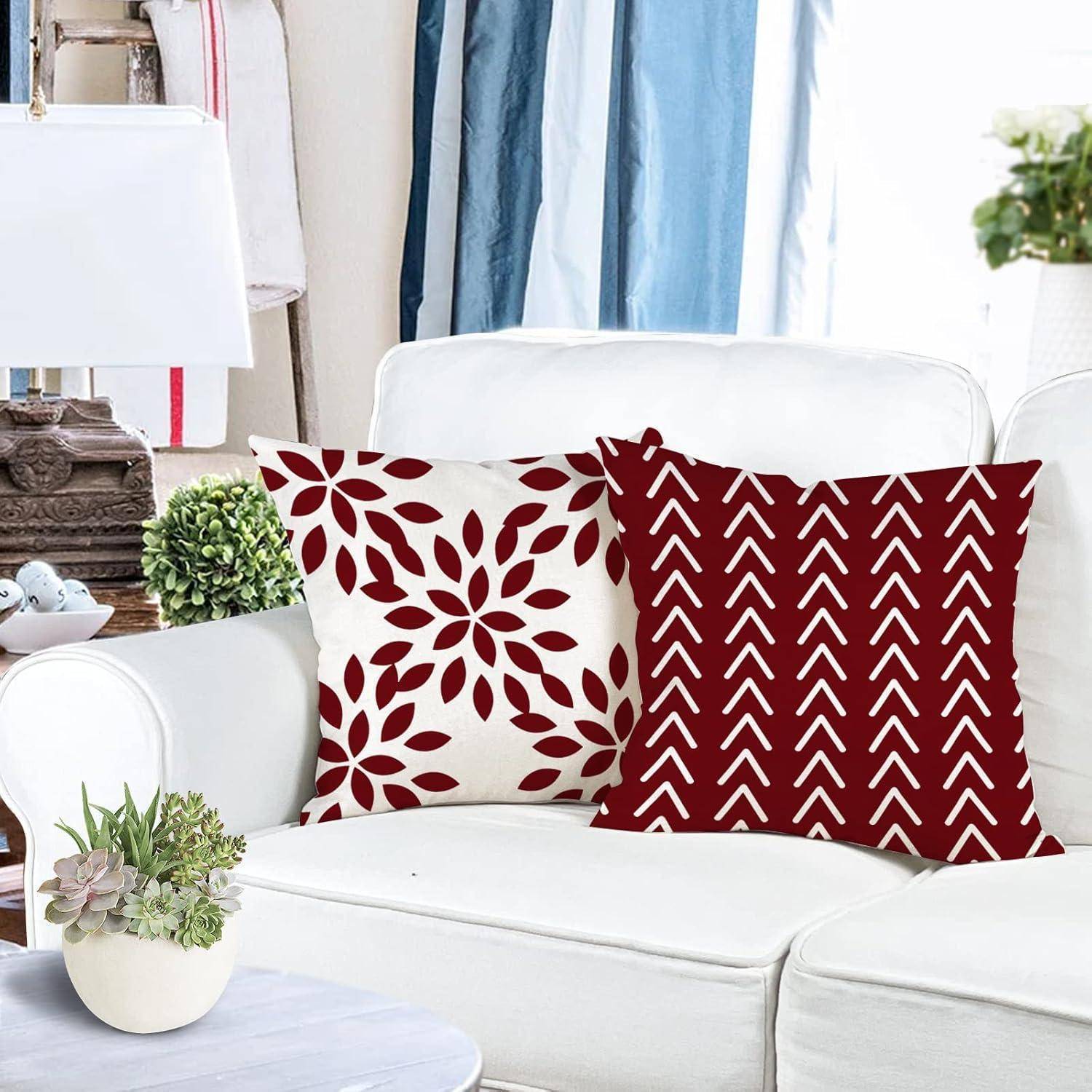Eine weiße Couch mit zwei rot-weiß gemusterten Kissen, eines mit Blattmotiven und das andere mit Zickzackmuster, umgeben von Zimmerpflanzen.