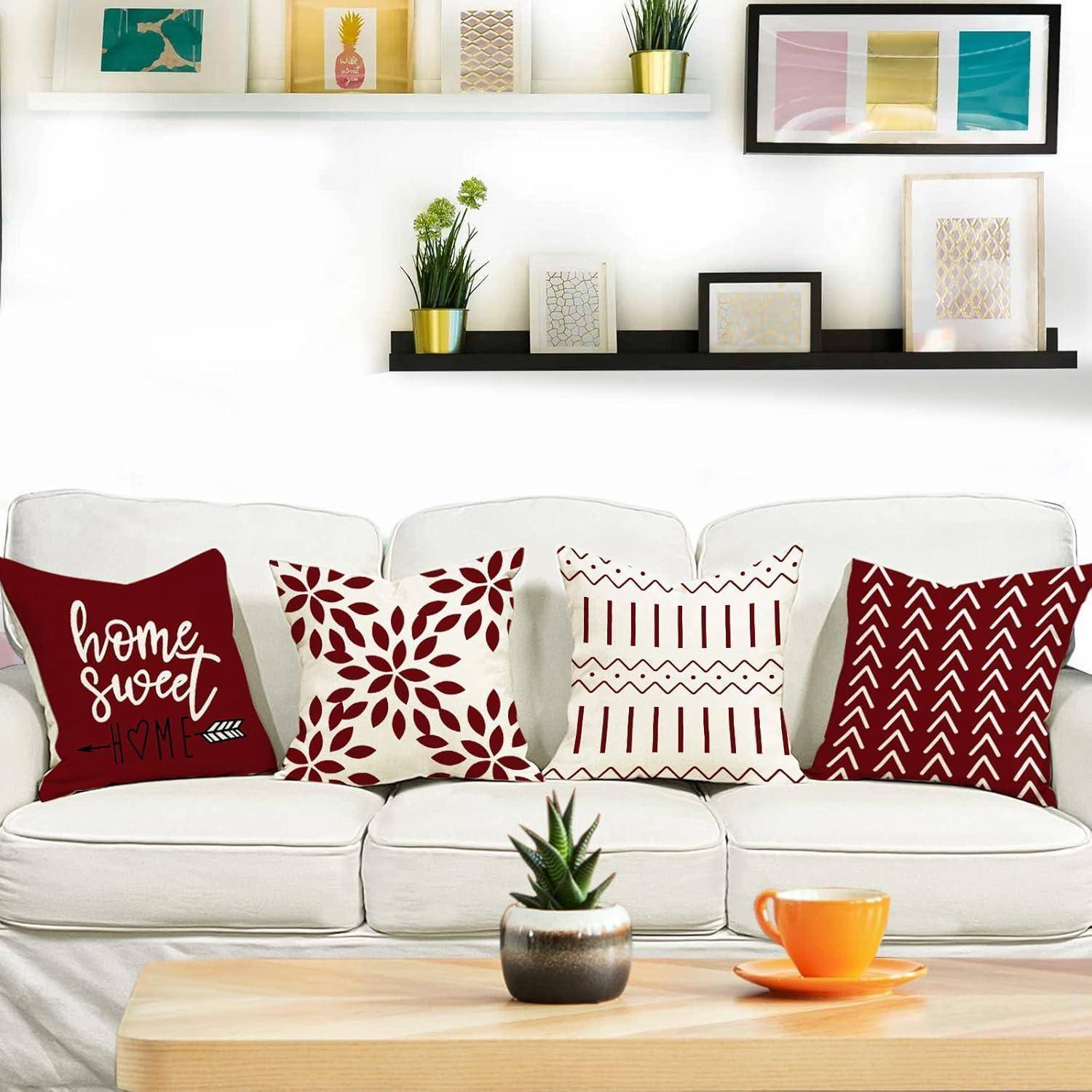 Ein weißes Sofa mit vier dekorativen Kissen, die jeweils ein rot-weißes Muster haben. Über dem Sofa hängen Regale mit Pflanzen und gerahmter Kunst.