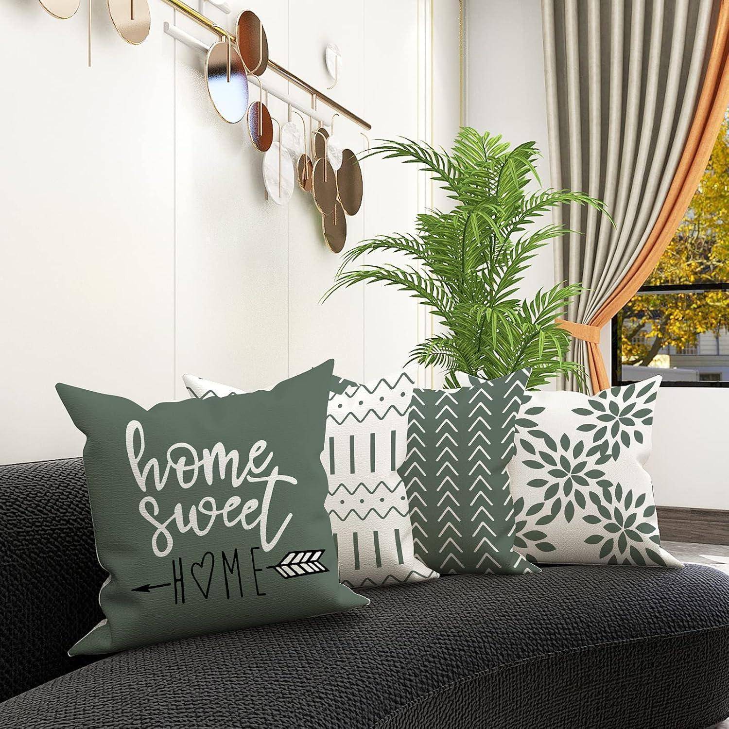 Ein gemütliches Wohnzimmer mit einem schwarzen Sofa, das mit dekorativen Kissen ausgestattet ist, darunter eines mit dem Text ‚Home Sweet Home', und einer Topfpflanze in der Nähe.